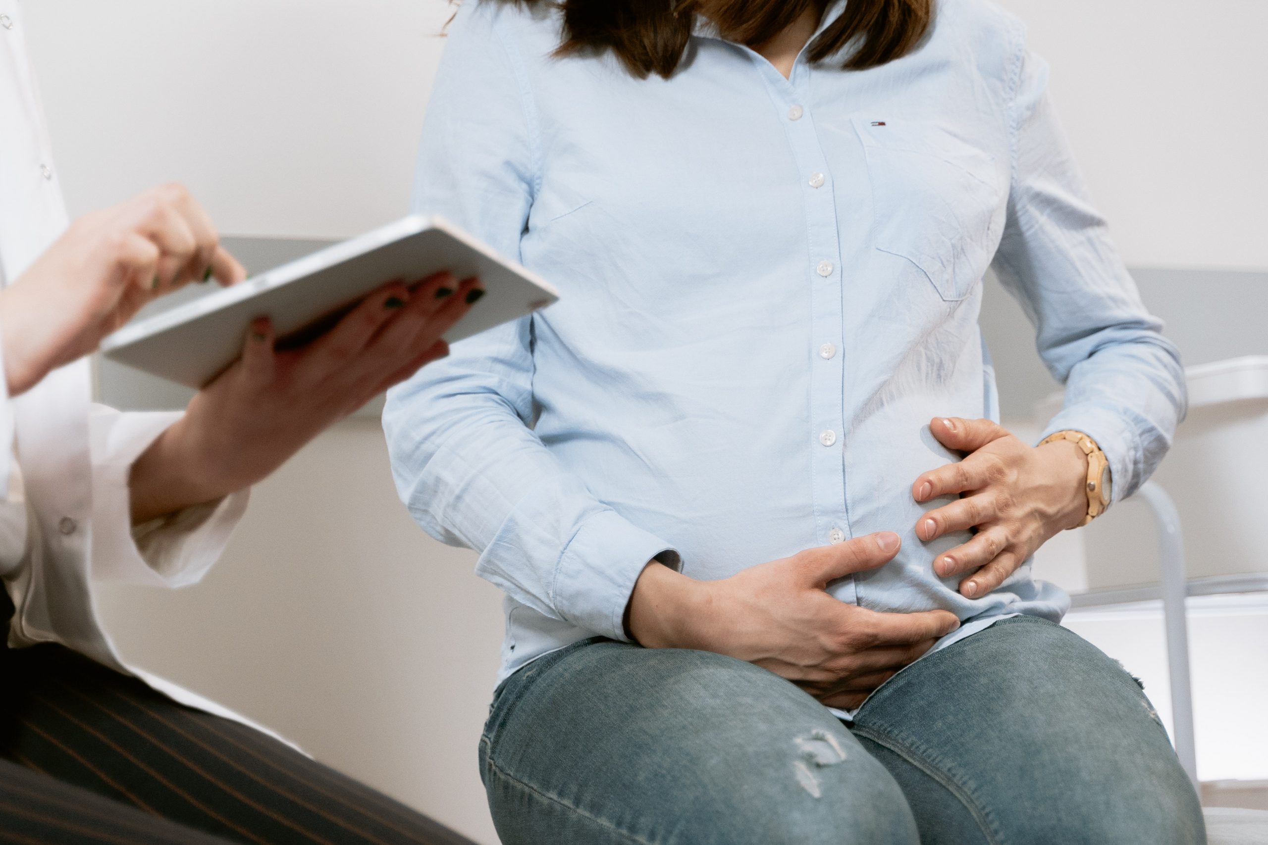 While waiting to be seen by her osteopath, a pregnant woman hugs her baby bump.