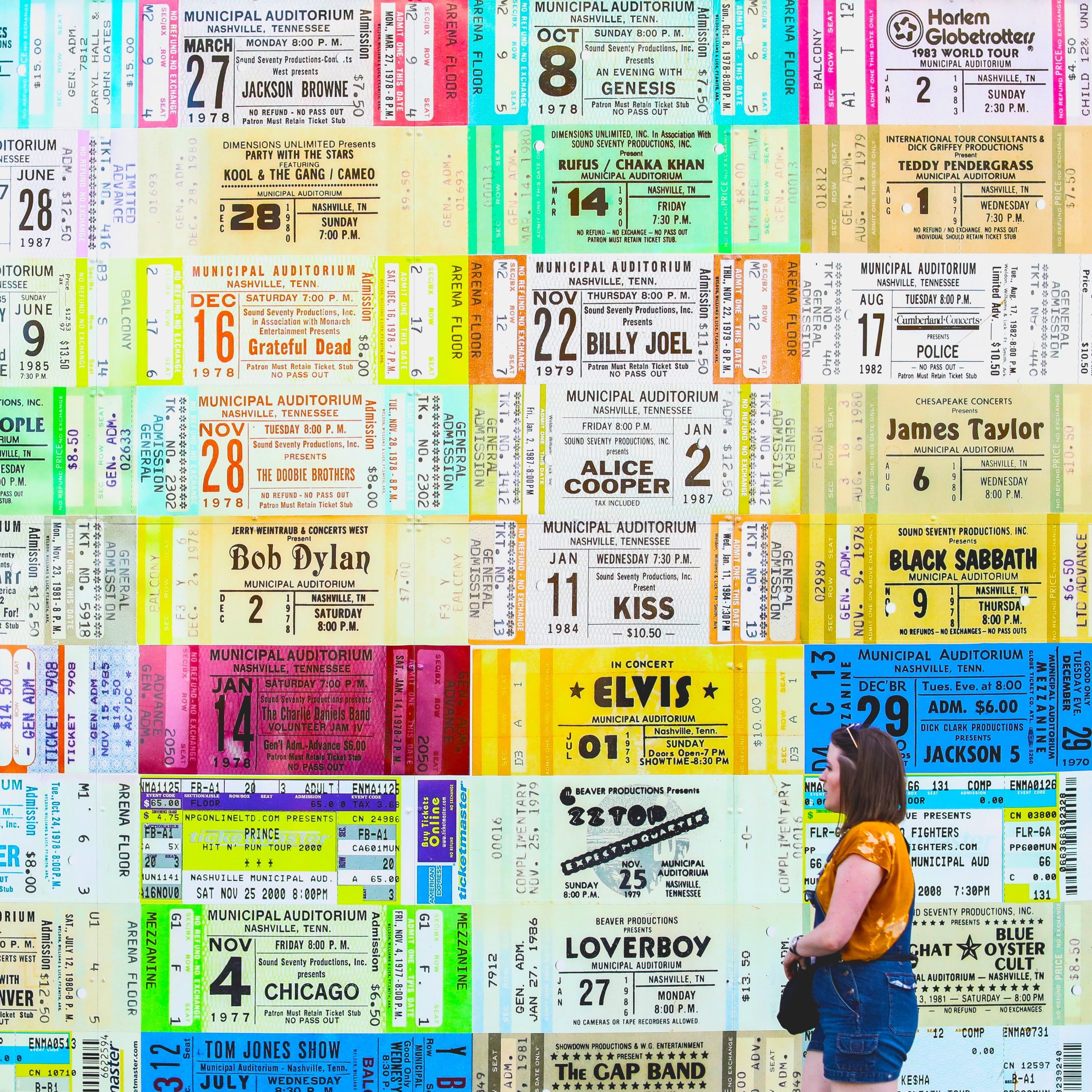 A woman looking up at a wall of giant concert and theatre tickets.