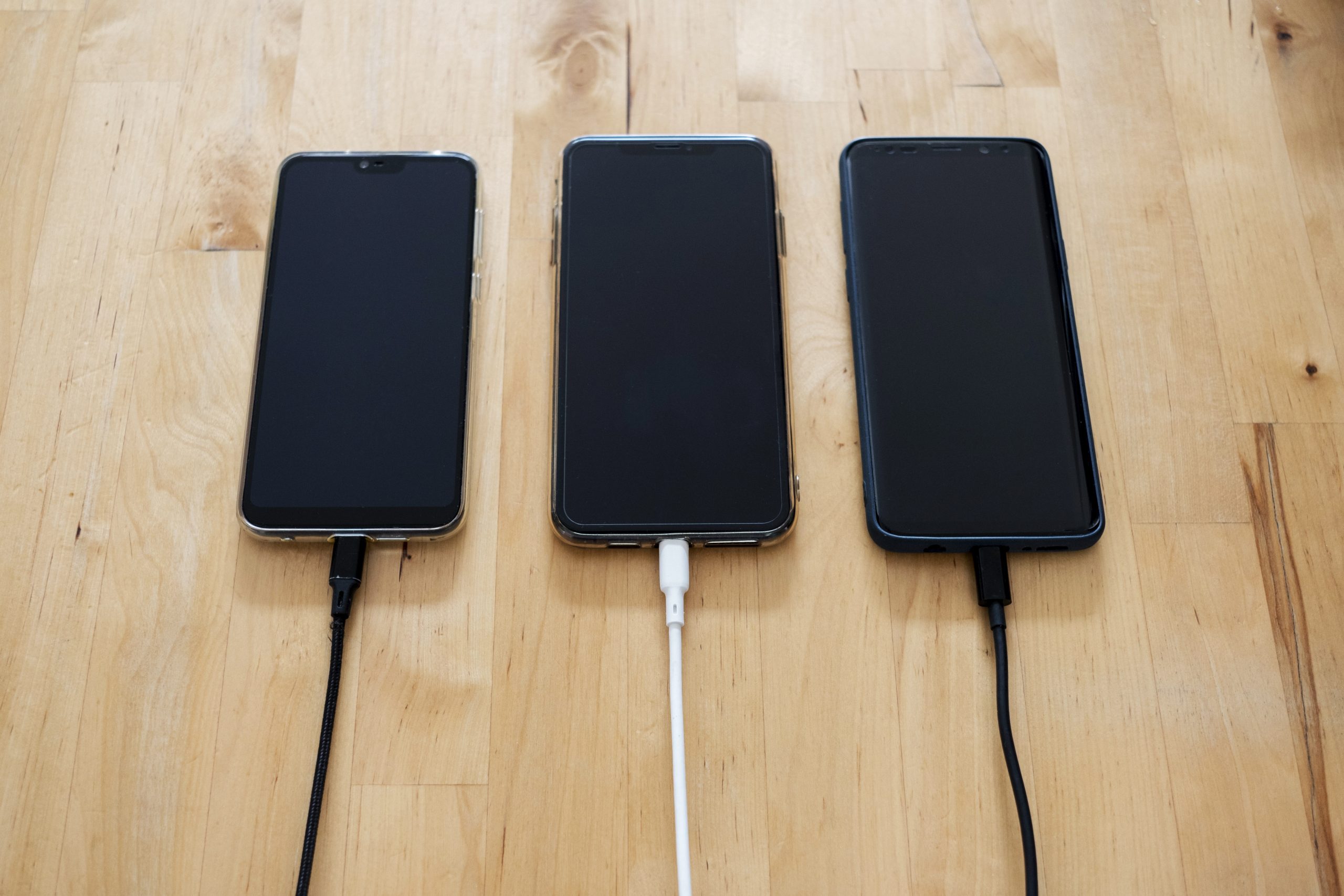 Three mobile phones being charged in an office.