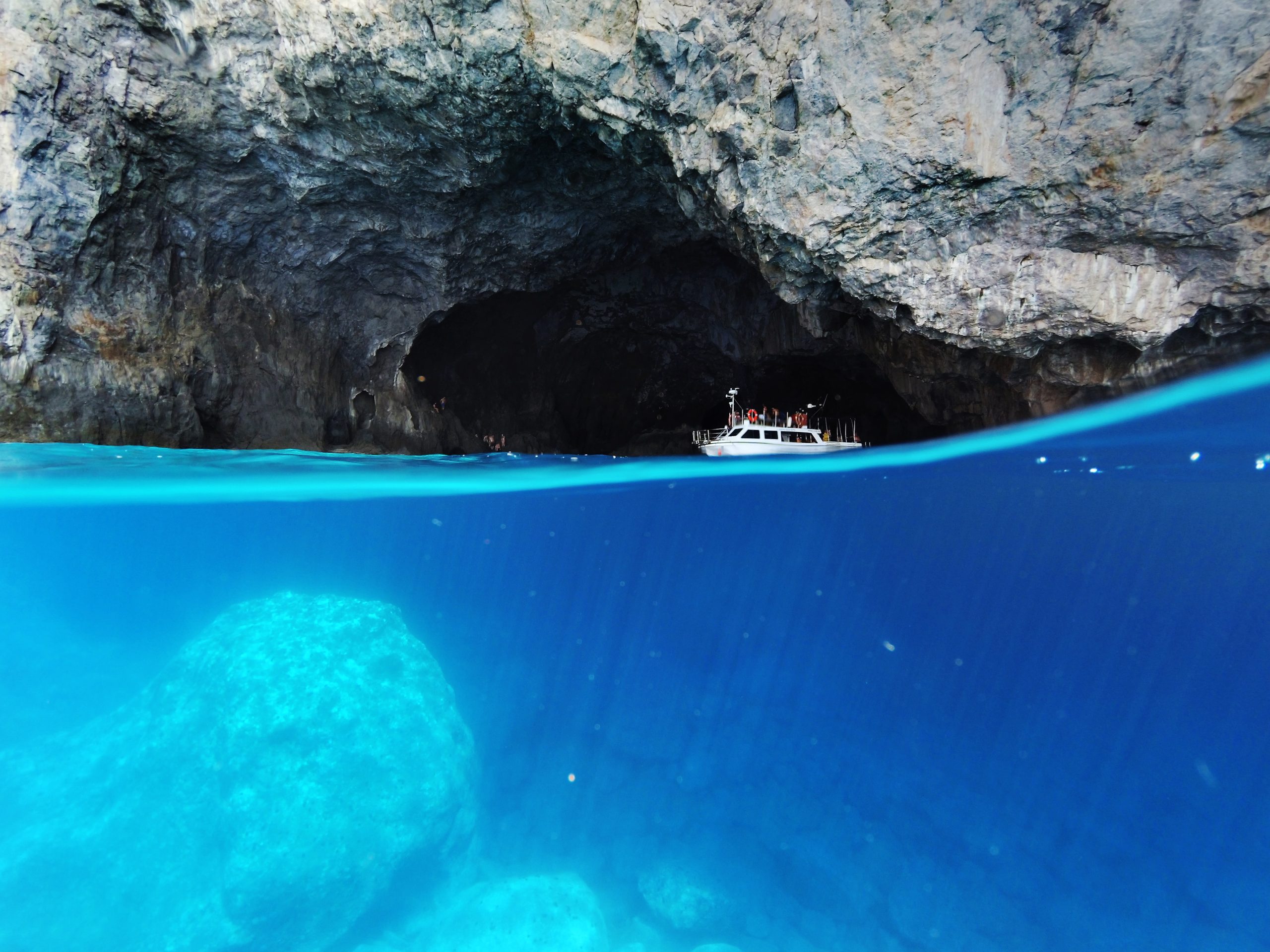 A boat sailing past a cave in crystal blue waters in Kythira, Greece.