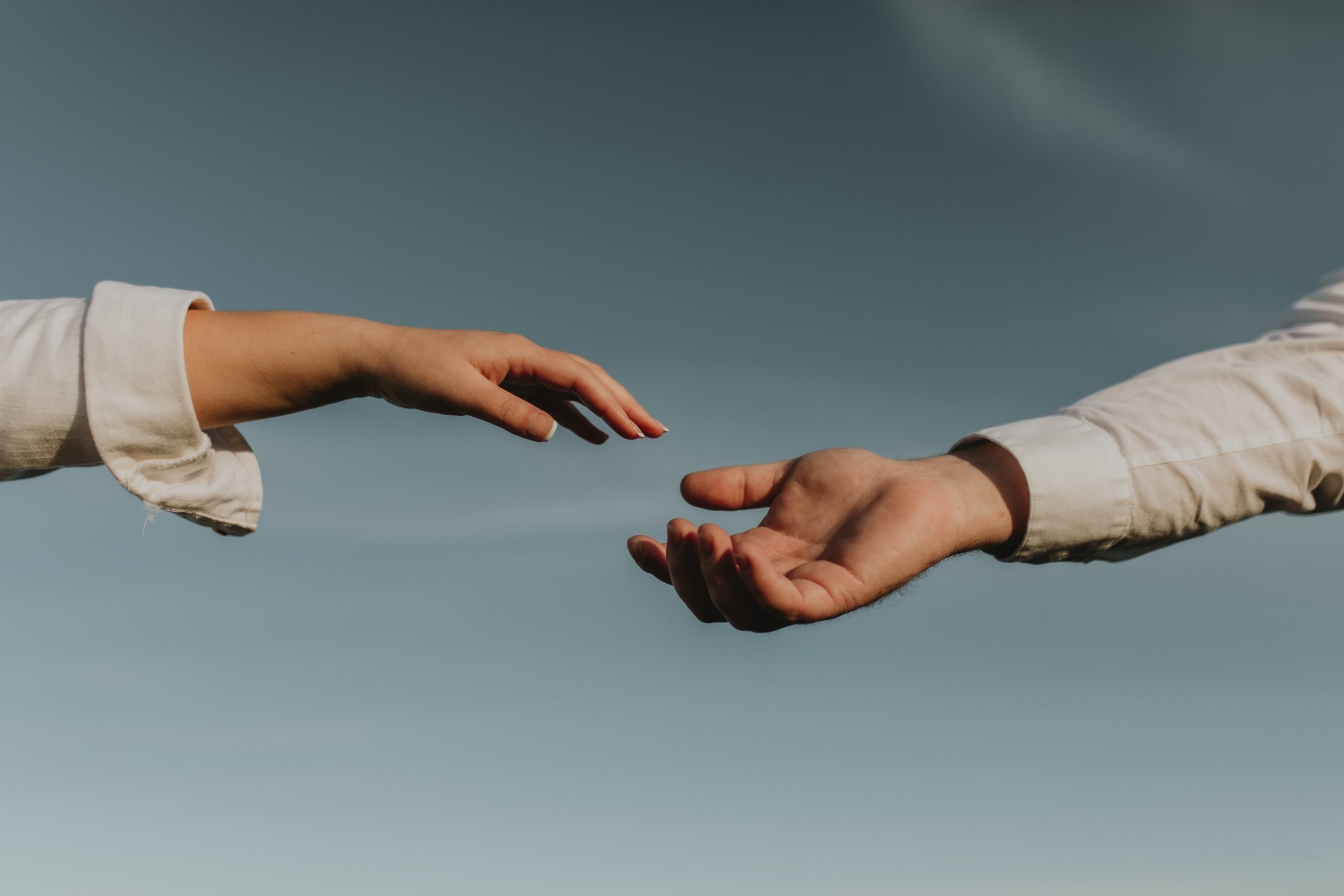 Two hands reaching towards each other against a blue sky.