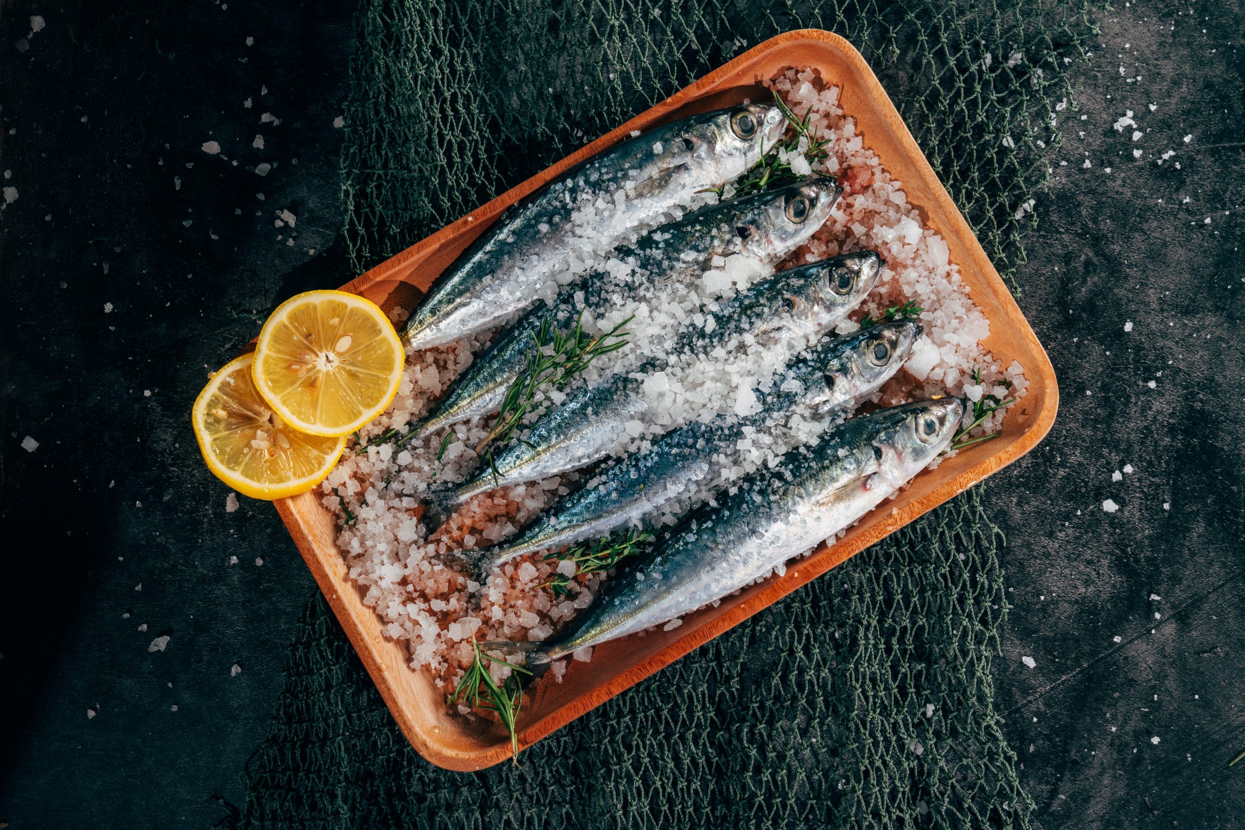 Five sardines on ice presented with two slices of orange.