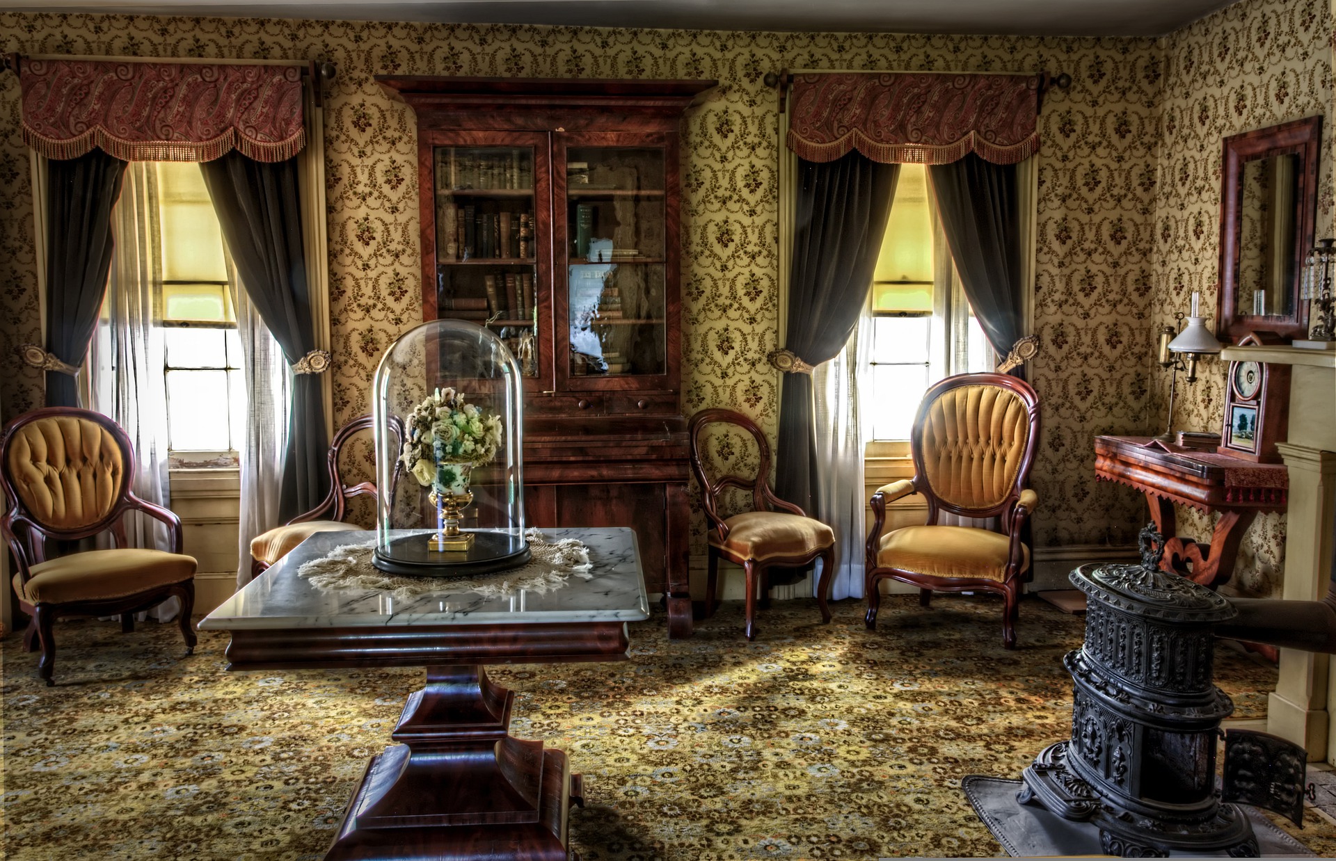 Victorian living room with velvet armchairs, patterned wallpapers and rugs, and dark green drapes 