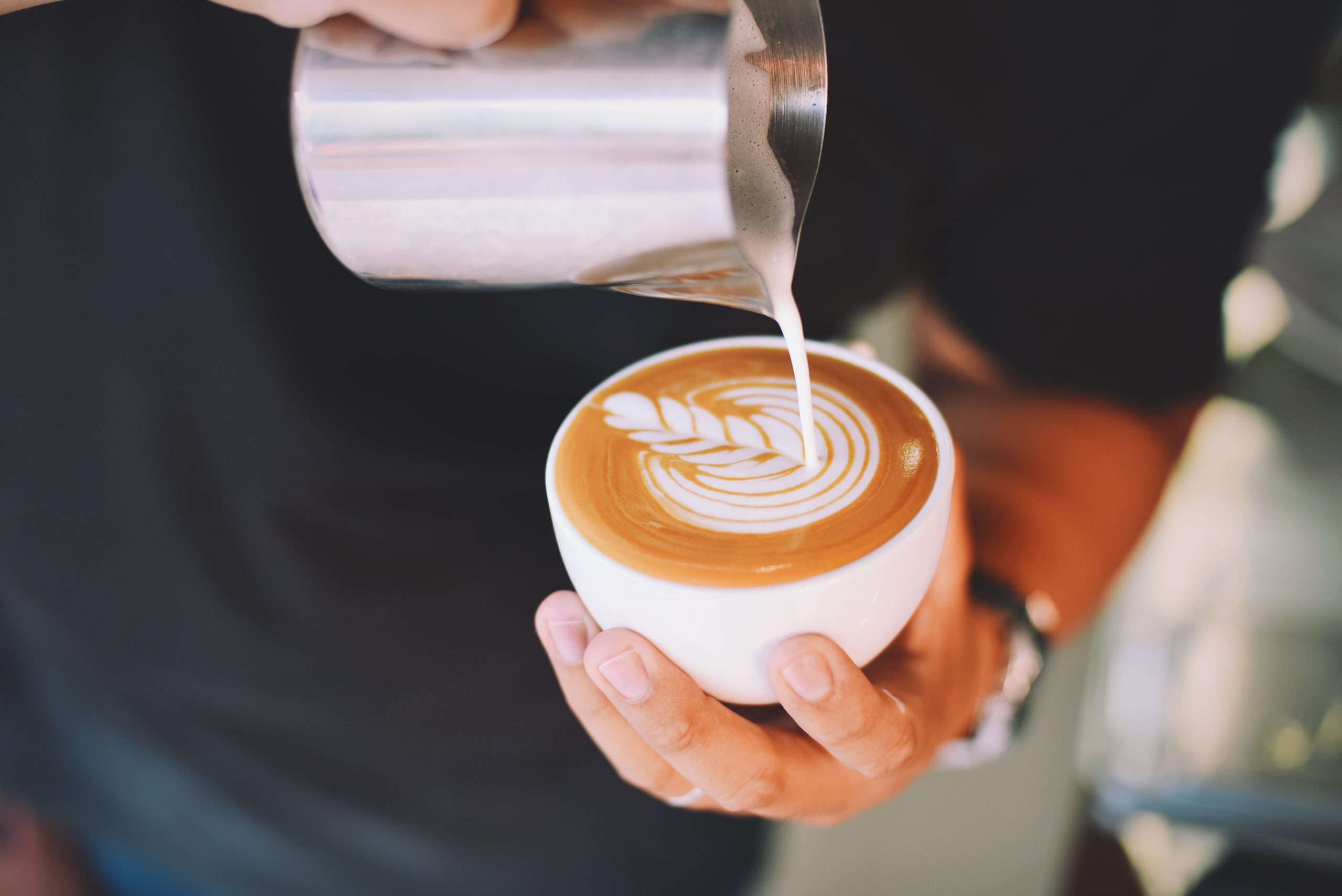 A steady hand pouring milk into a pumpkin spiced latte to create foam art in the froth.