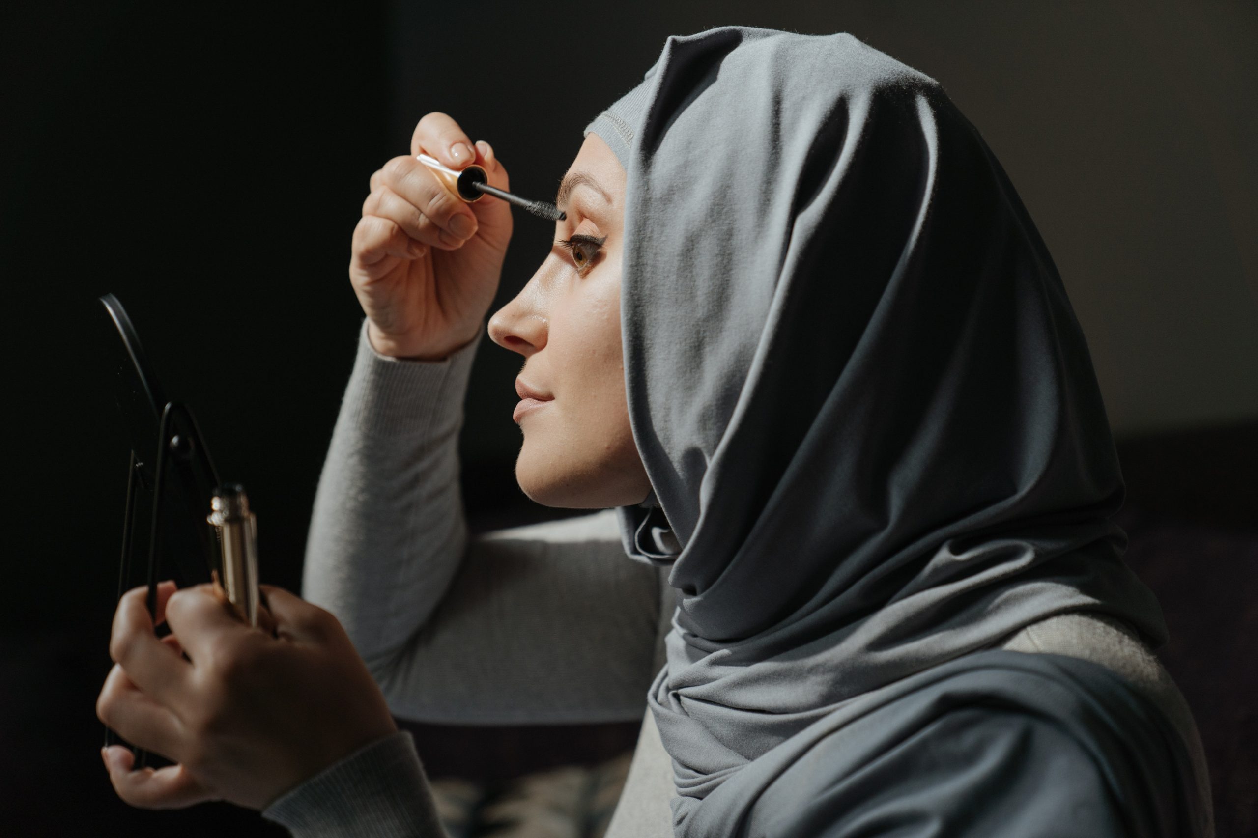 Woman wearing grey hijab applies a waterproof mascara