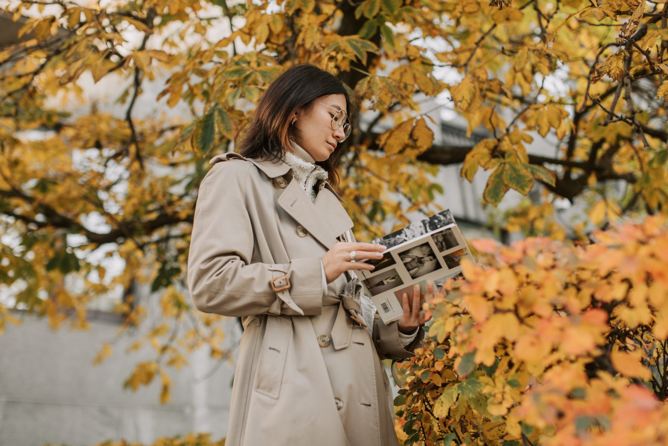 A young Asian woman reading the back cover of her book while walking in the park.