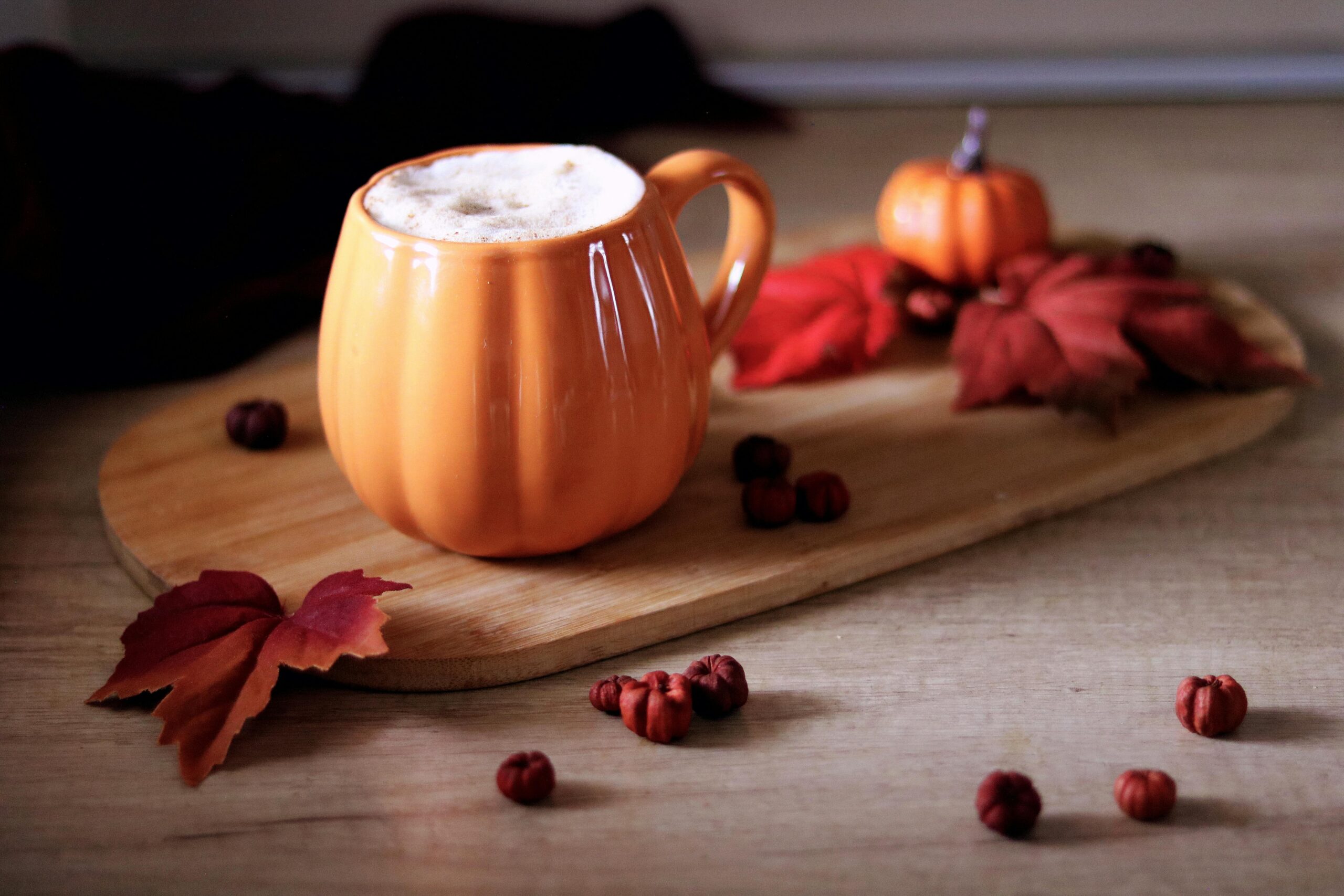 Pumpkin spice latte in a pumpkin shaped mug surrounded by autumnal decorations