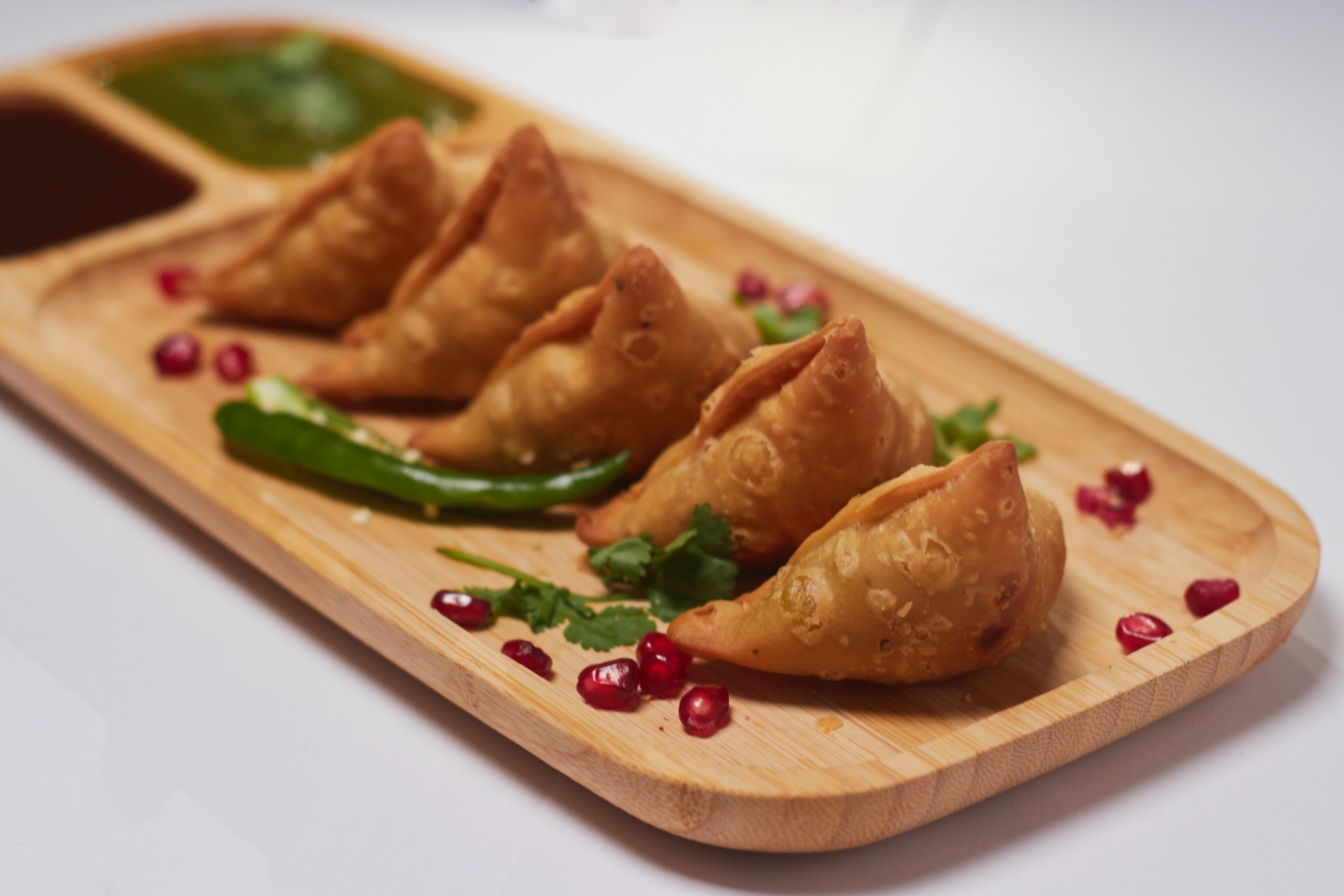 A platter of samosas, sprinkled with coriander and pomegranate seeds.