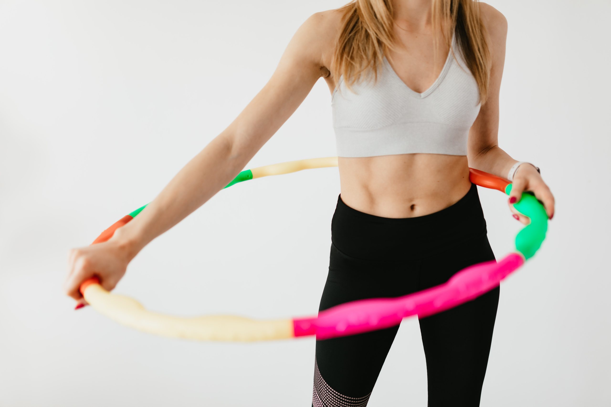 A young woman hula-hooping in a white studio.