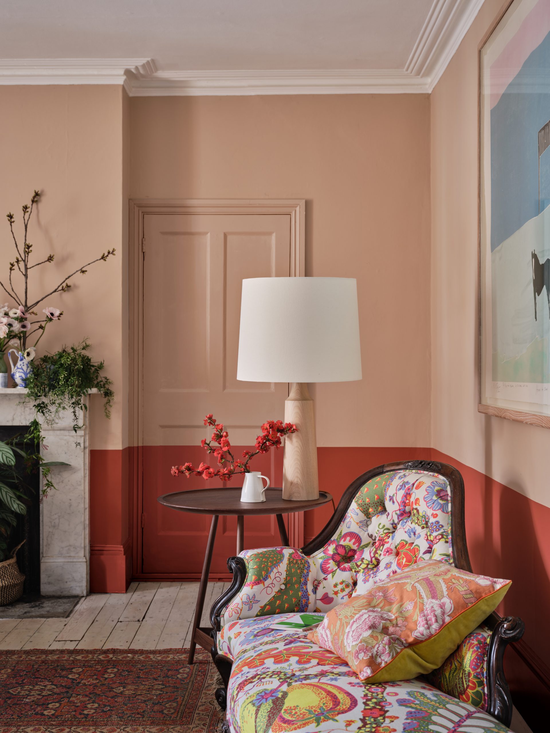 Living area with floral patterned armchair, small black round table, pastel pink lamp and pastel pink wall