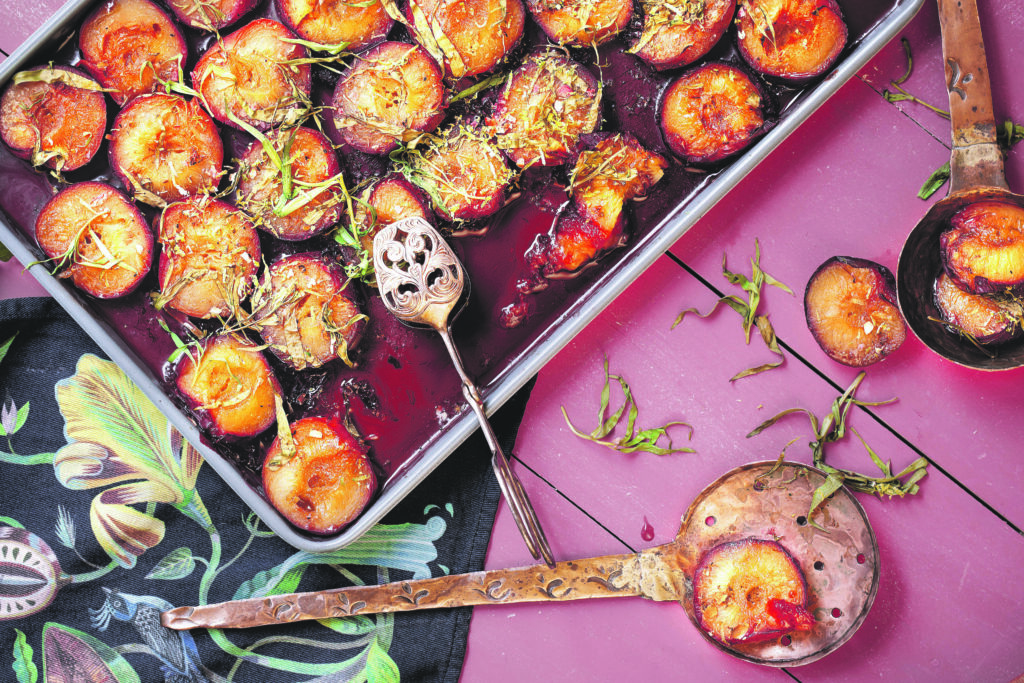 Baked plums with honey and cinnamon in a baking tray on old wood pink table with retro style spoon from above
