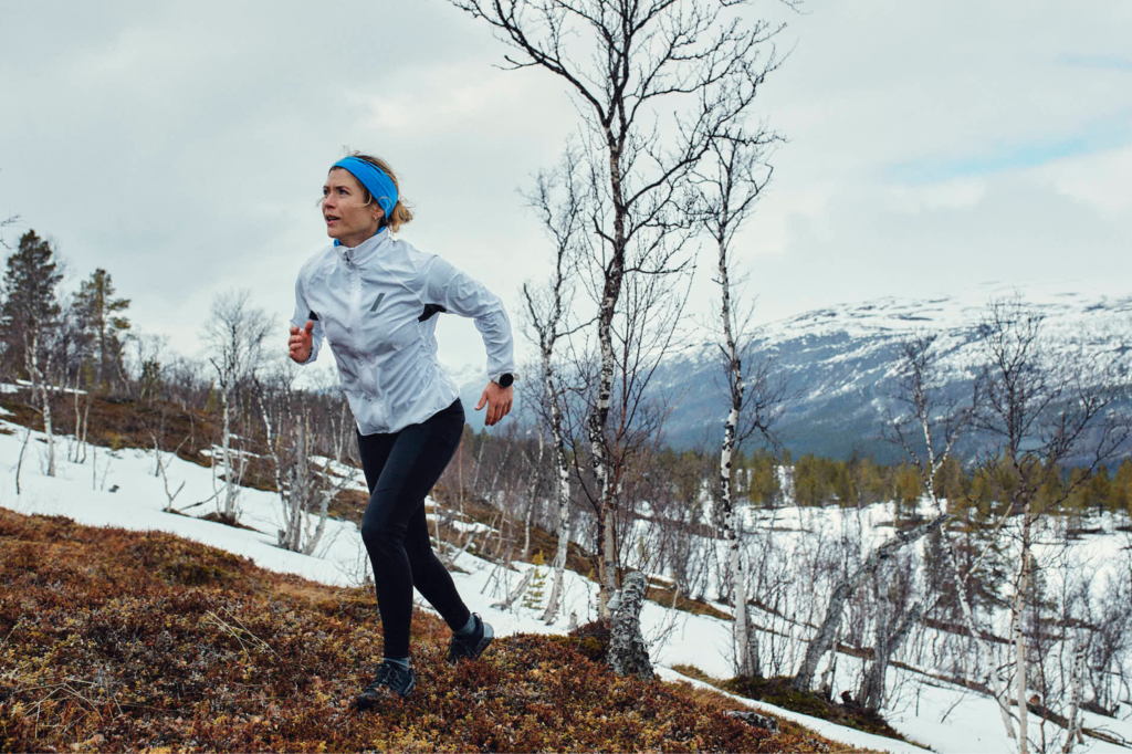 A middle-aged woman jogs through a snow-covered hill.