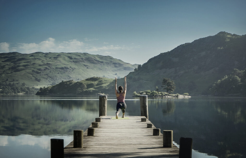 A woman practising yoga on a pier overlooking a lake in the Lake District, UK.