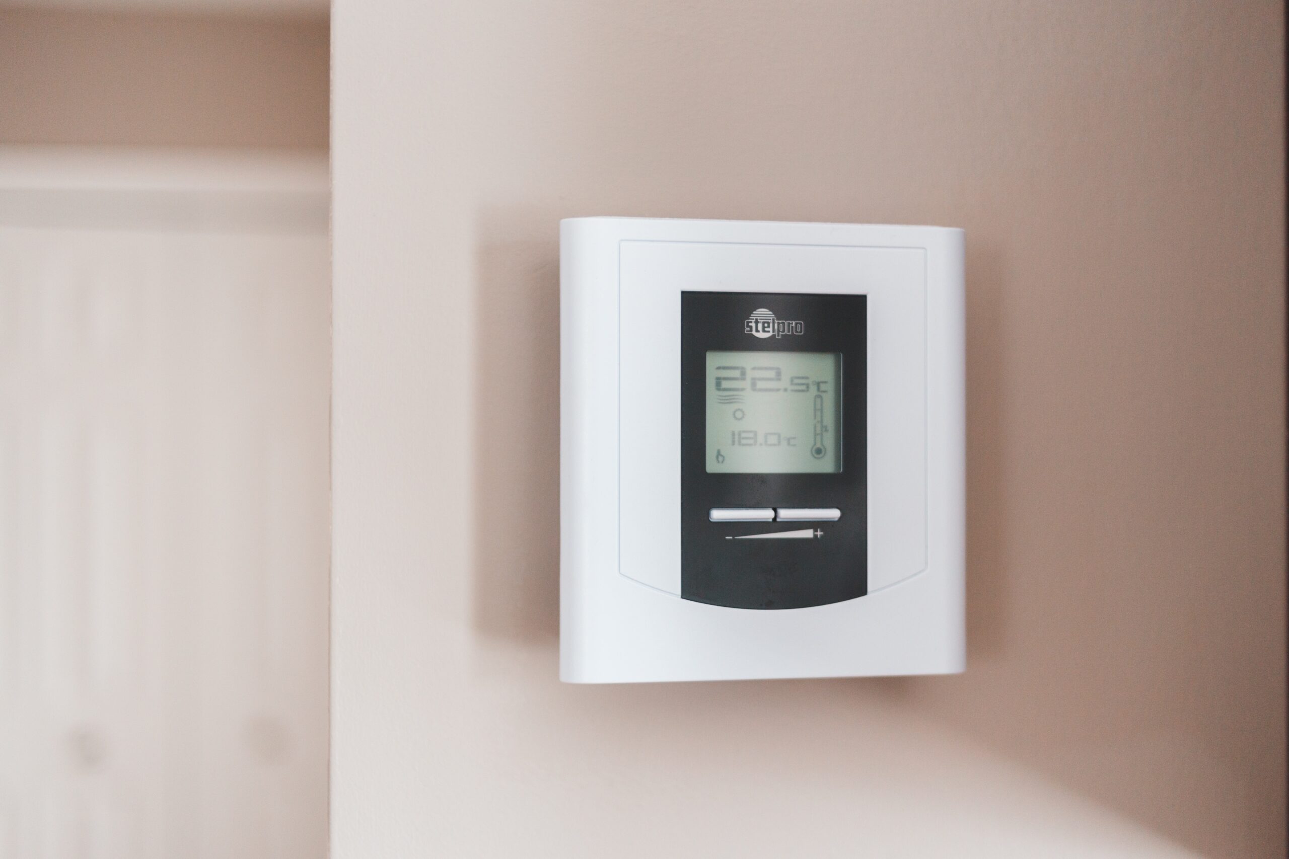 A white thermostat on a living room wall controls the room temperature.