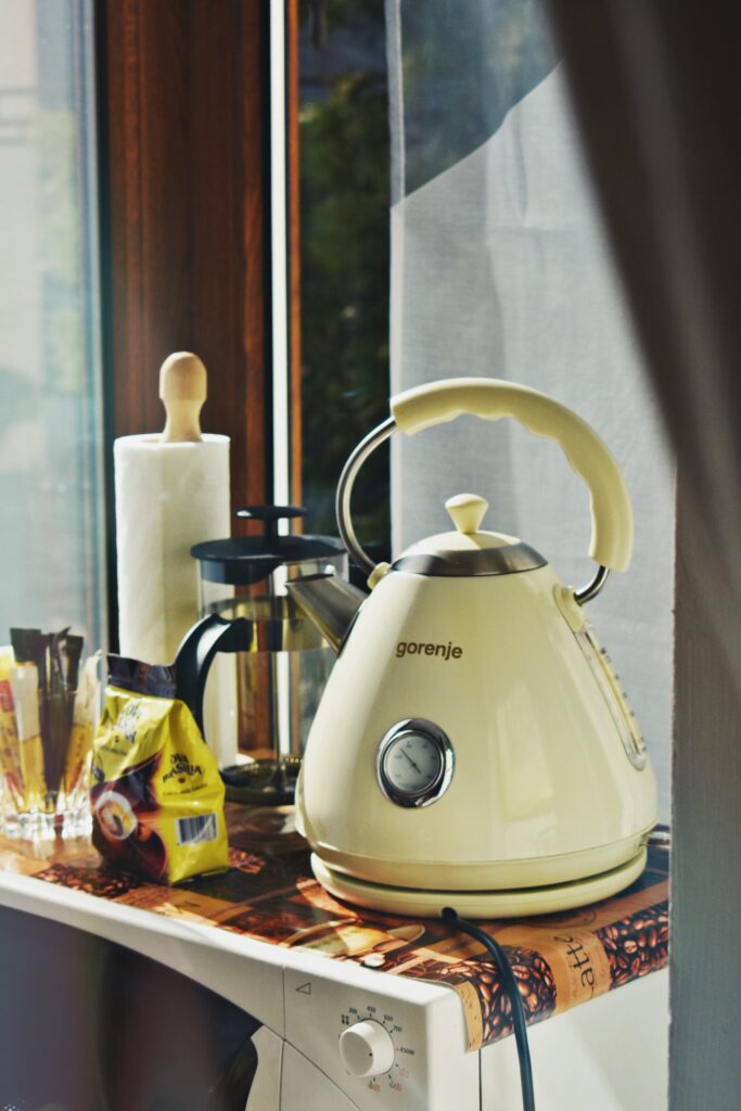 A beige Gorenje electric kettle with a temperature regulator and water level indicator sitting atop a microwave next to a window.