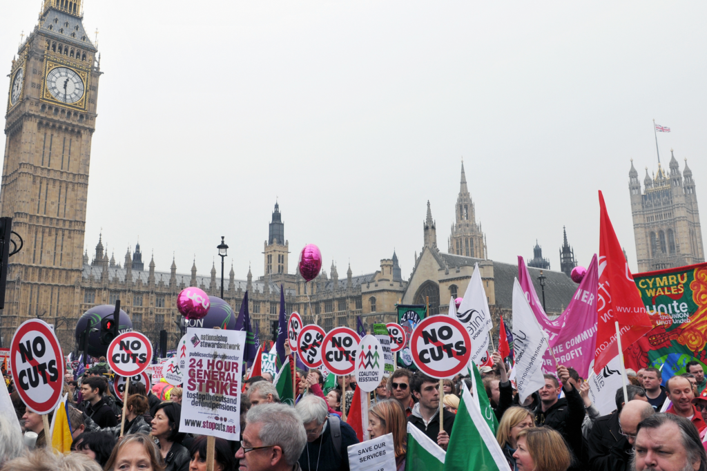 A crowd protesting against government cuts outside the Houses of Parliament.