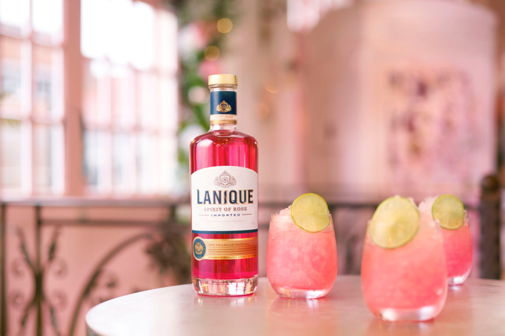 A bottle of Lanique Spirit of Rose, made from the pure essence of roses, next to three cocktails made from it.