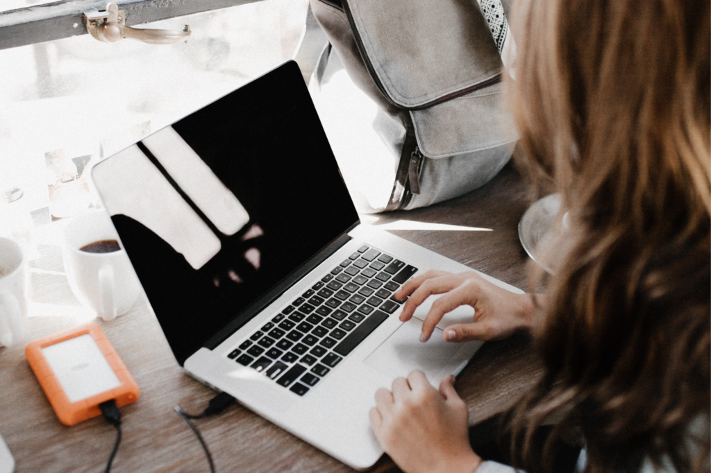 A young woman updates her CV on her MacBook at her desk.