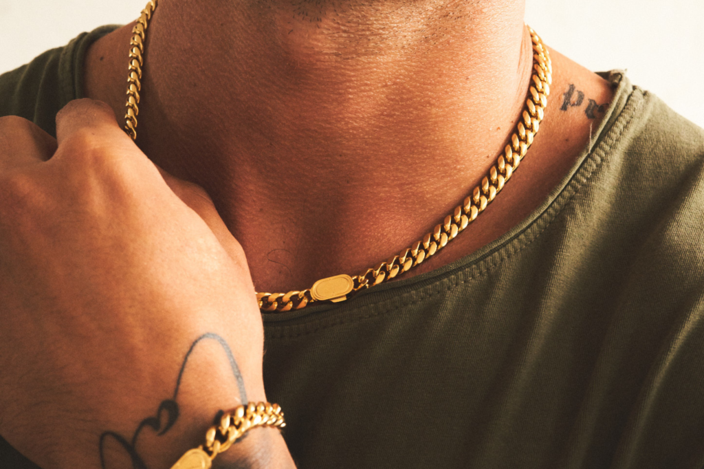 A gold Abbott Lyon Signature Name Necklace being worn by a man with tattoos. 