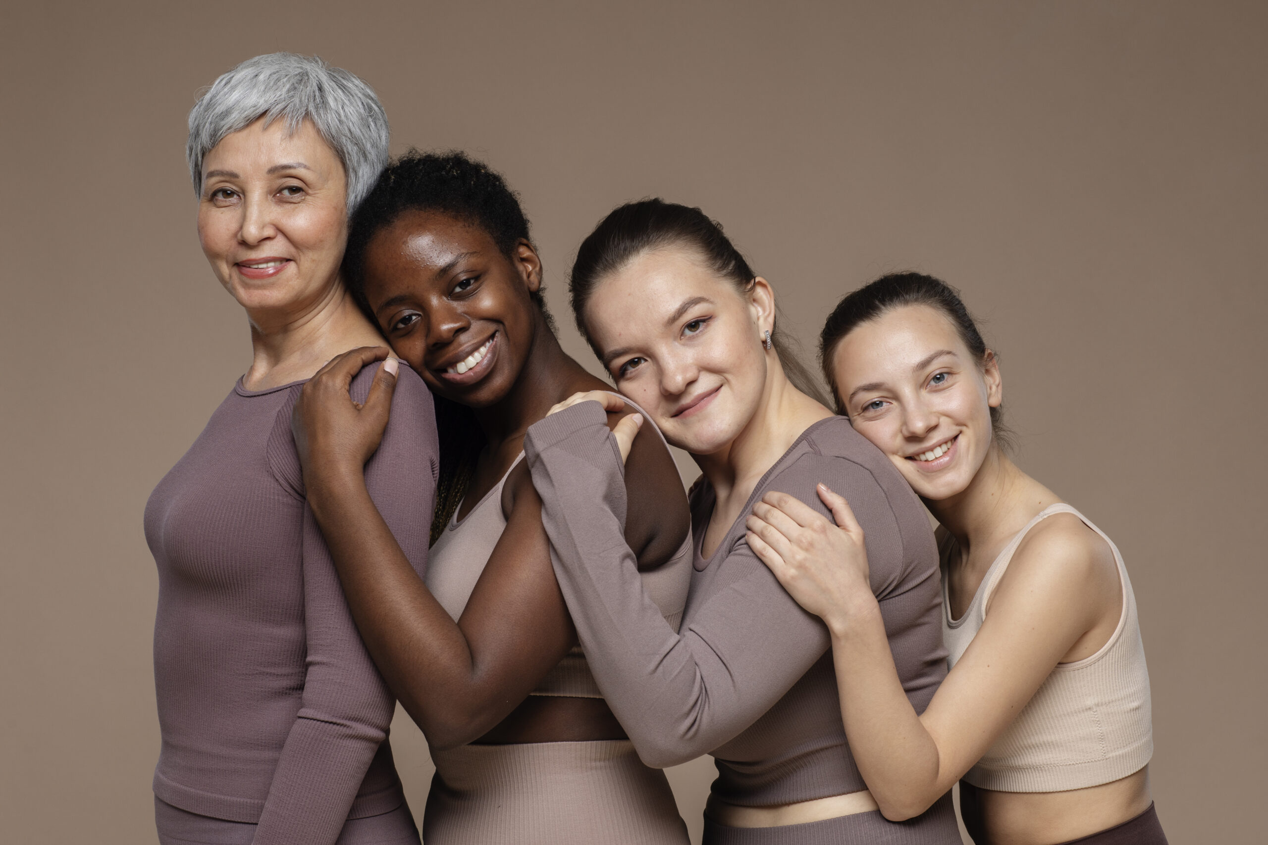 Four women of different ages and races stand in a row holding each other