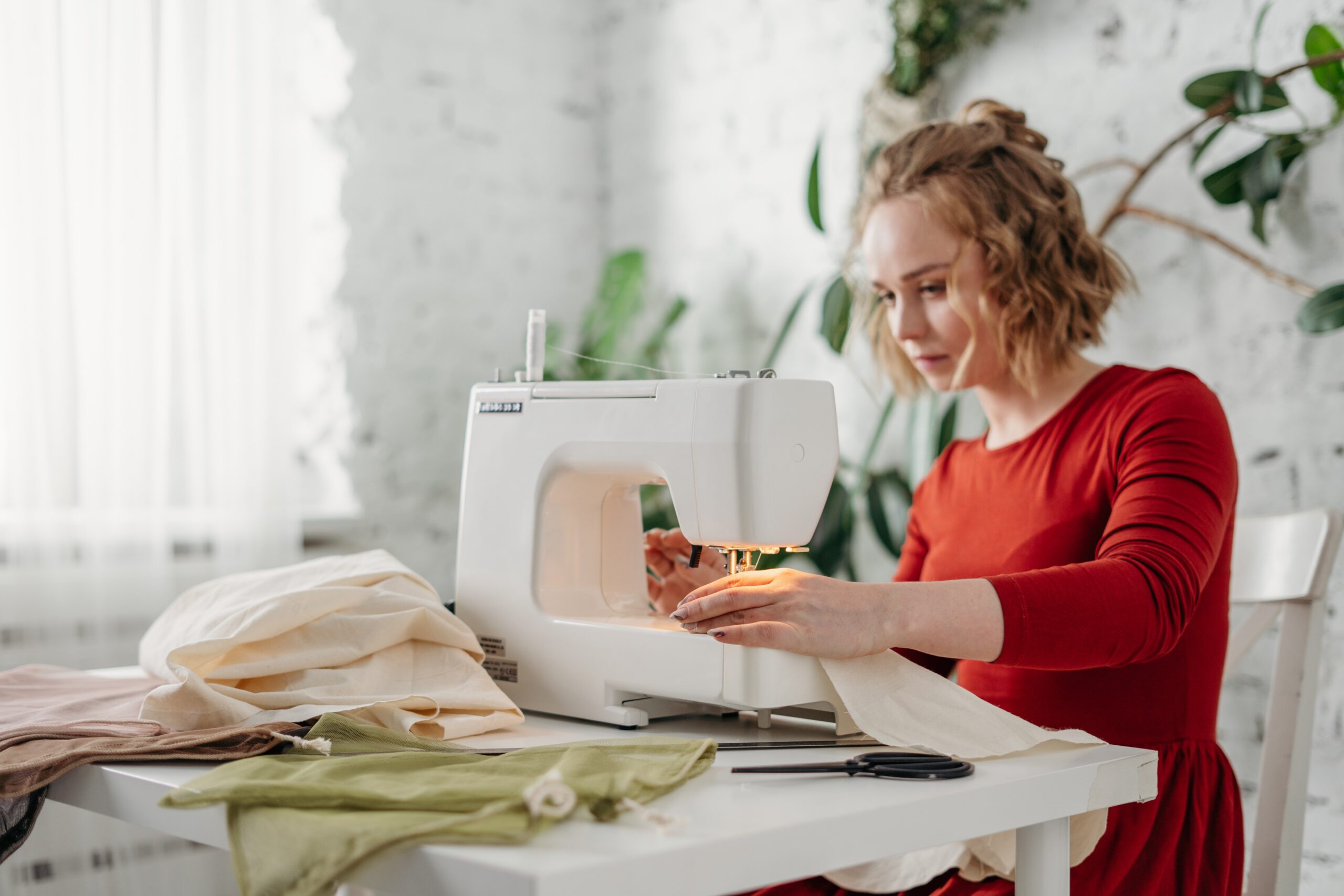 A young woman in red making a dress with a sewing machine.