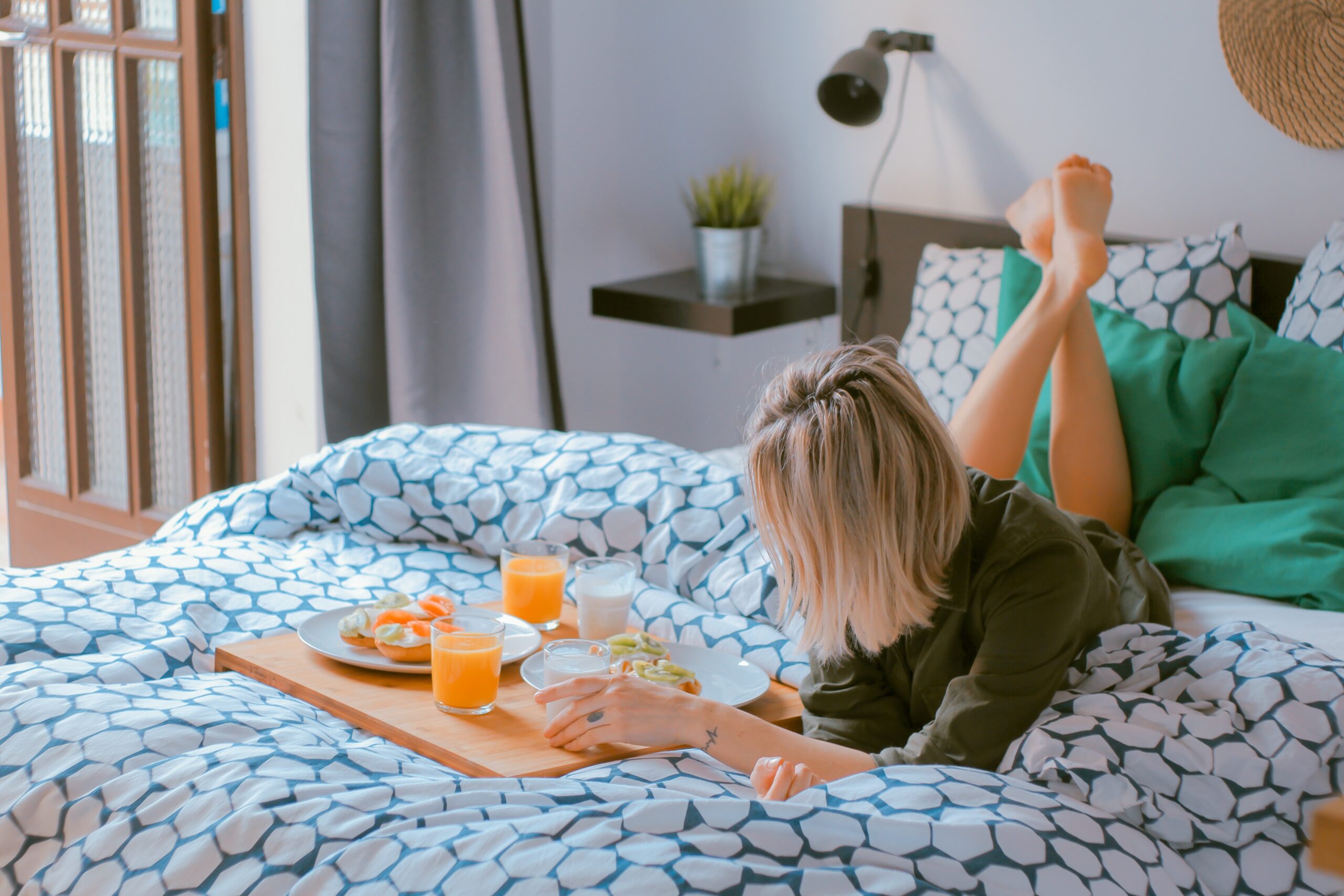 Stretched out on top of the sheets, a young woman enjoys breakfast in bed.