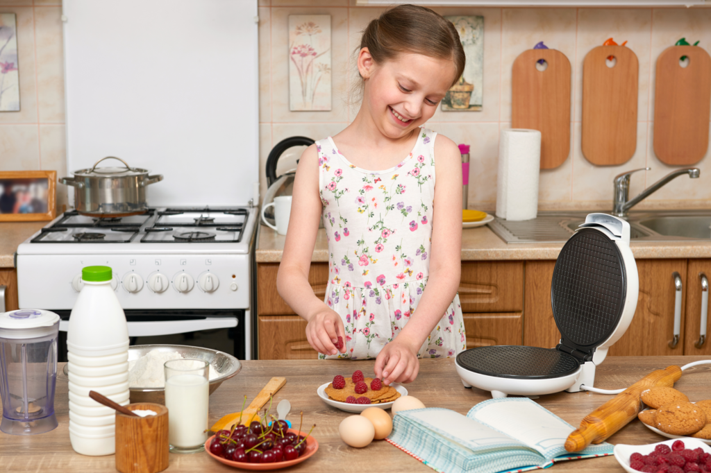 A teenage girl in a flowery dress making pancakes in the kitchen.