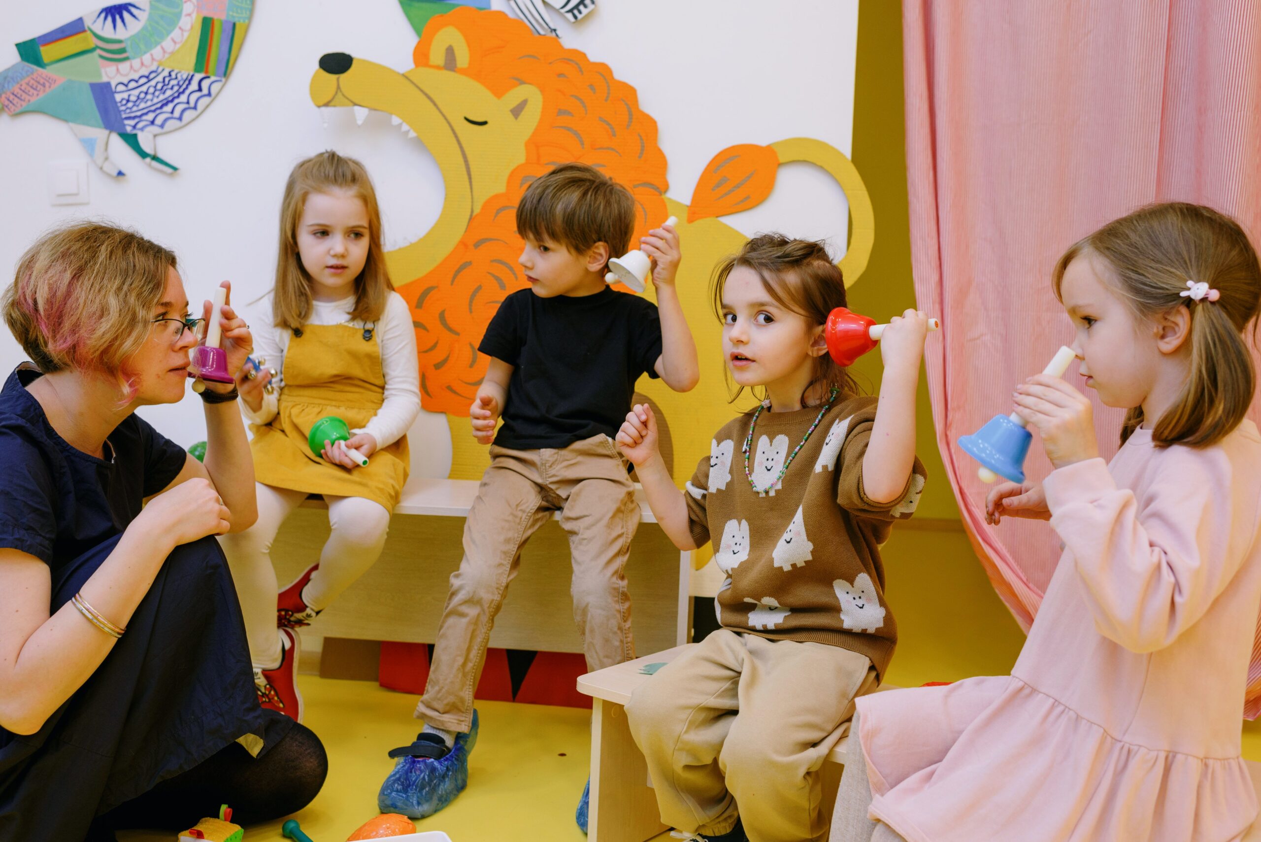 Children holding bells, playing with their teacher.