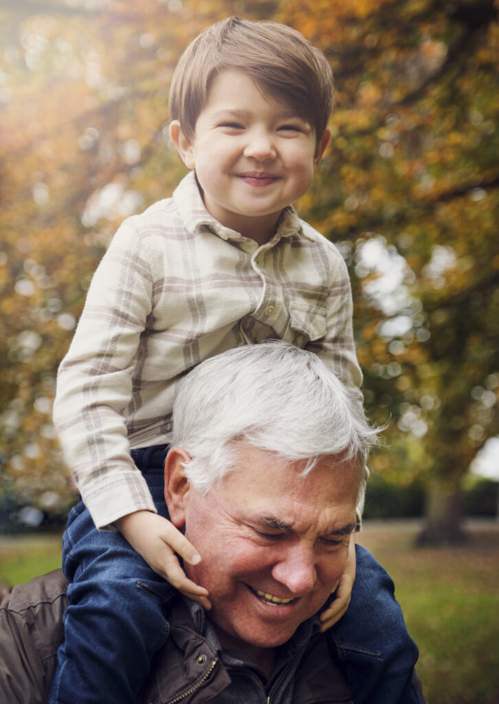 Smiling boy sitting on grandfather's shoulder at park