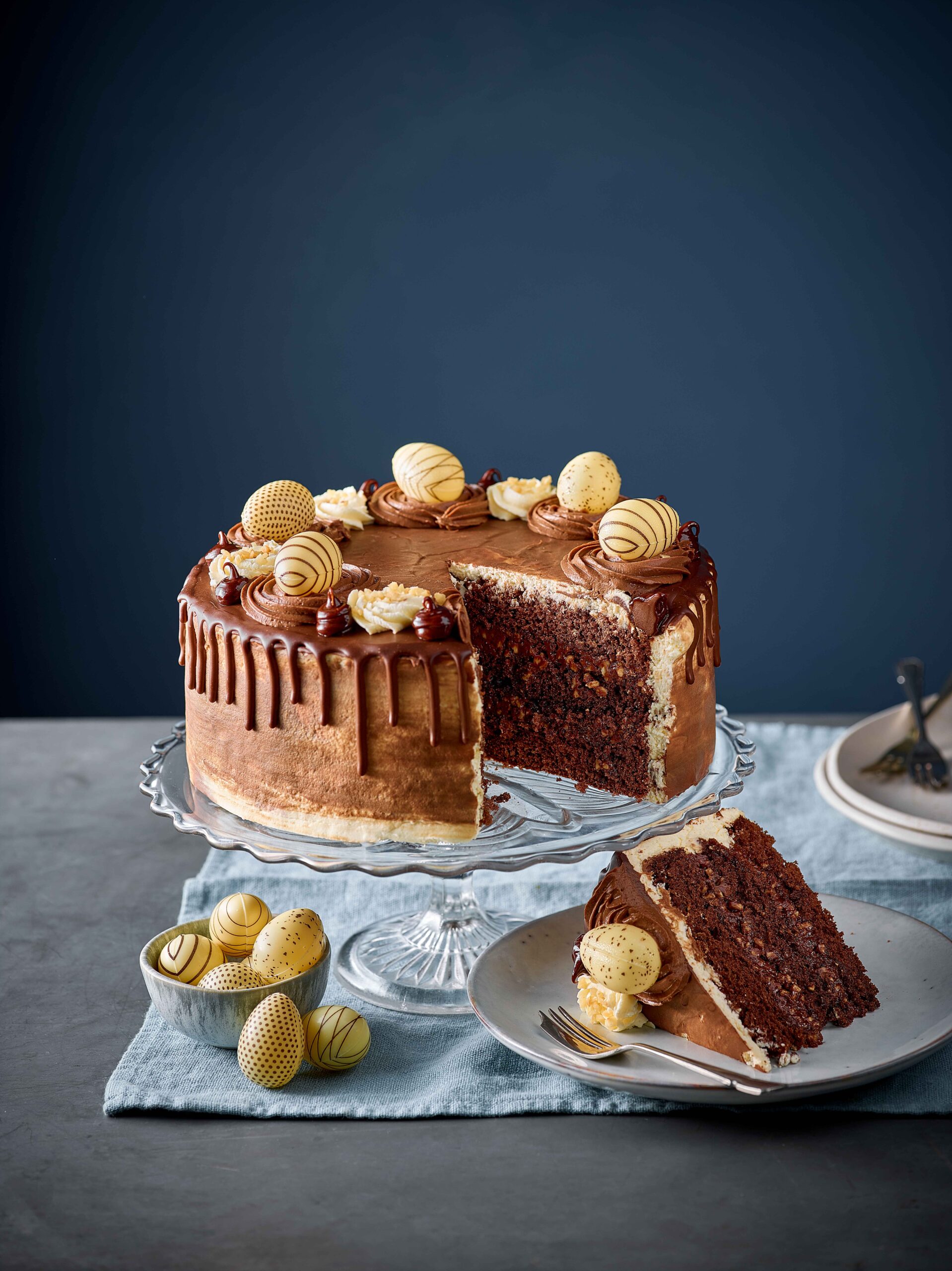 A slice of Patisserie Valerie’s Nutella Easter Nest Cake served next to a bowl of chocolate easter eggs.