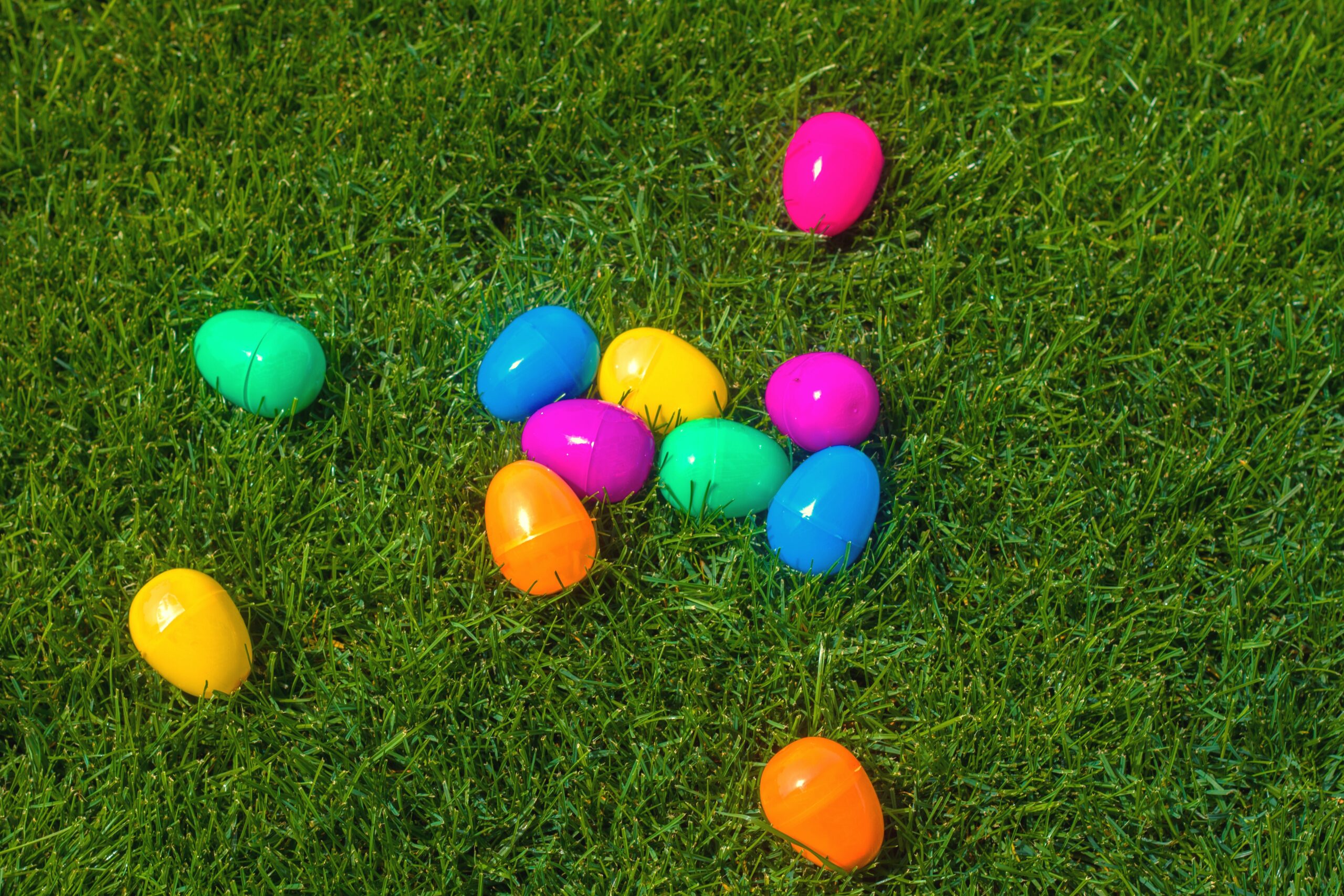 A selection of multi-coloured Easter eggs from a scavenger hunt lying in the grass in a park.