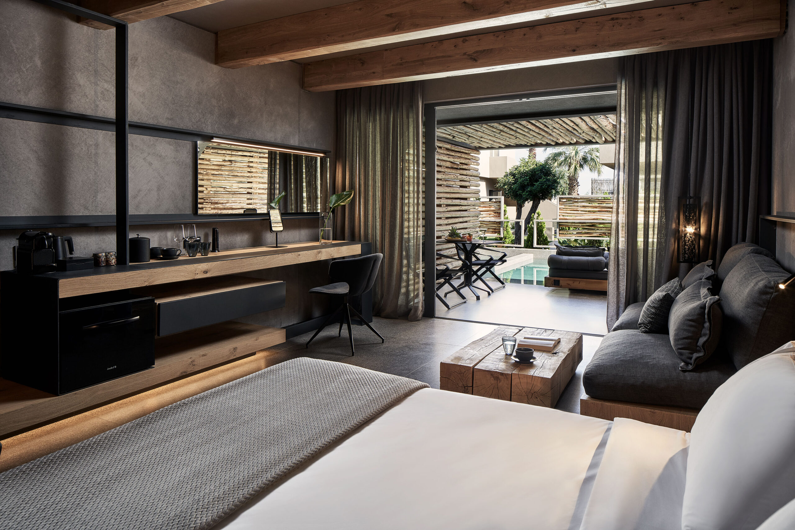 Hotel room with bed, wooden floors and balcony with pool in the distance