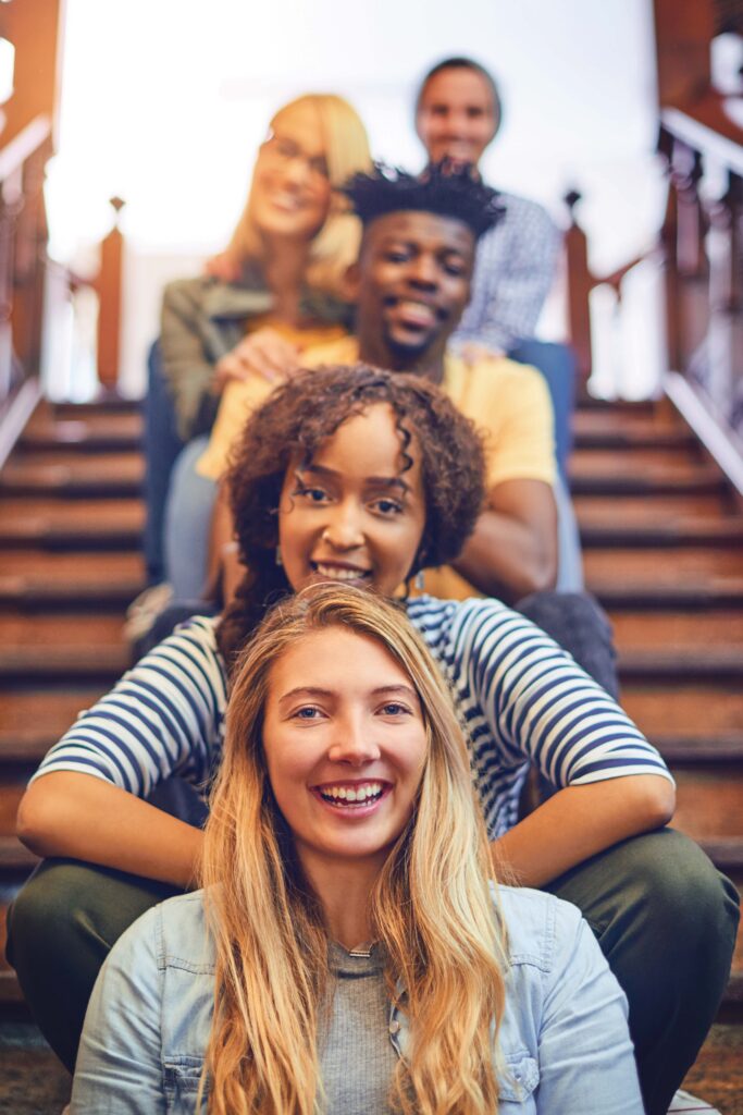 Portrait of a group of diverse university students sitting in a row on the staircase on campus