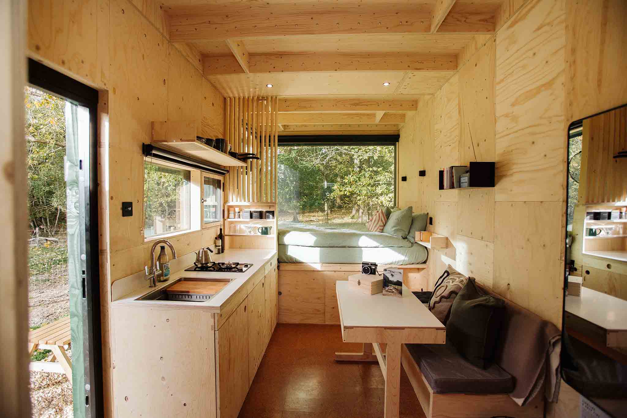 Interior of little cabin with bed, kitchen and table, surrounded by nature.