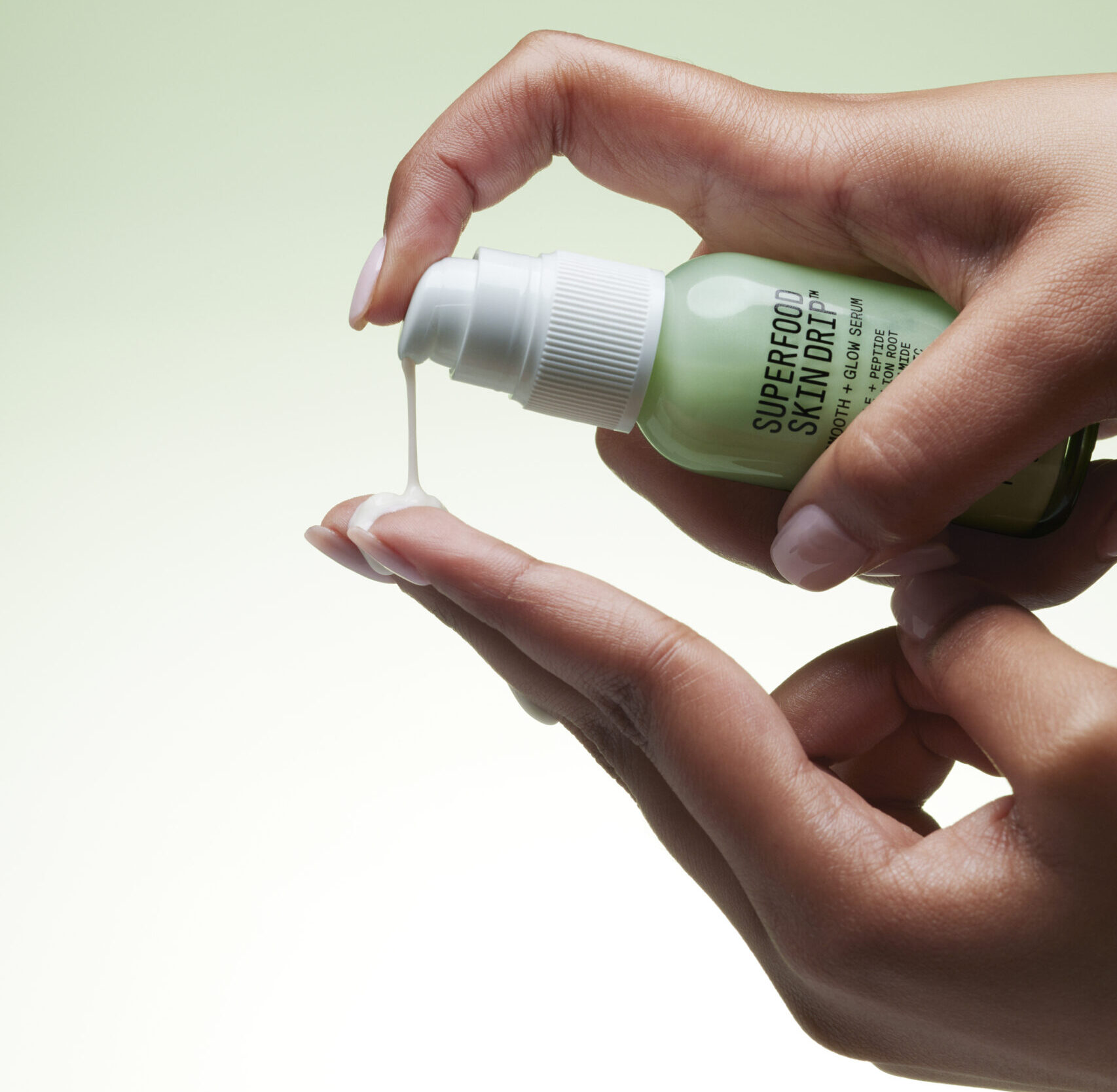 Two hands release serum out of a bottle of Youth to the People Superfood Skin Drip Smooth + Glow Serum