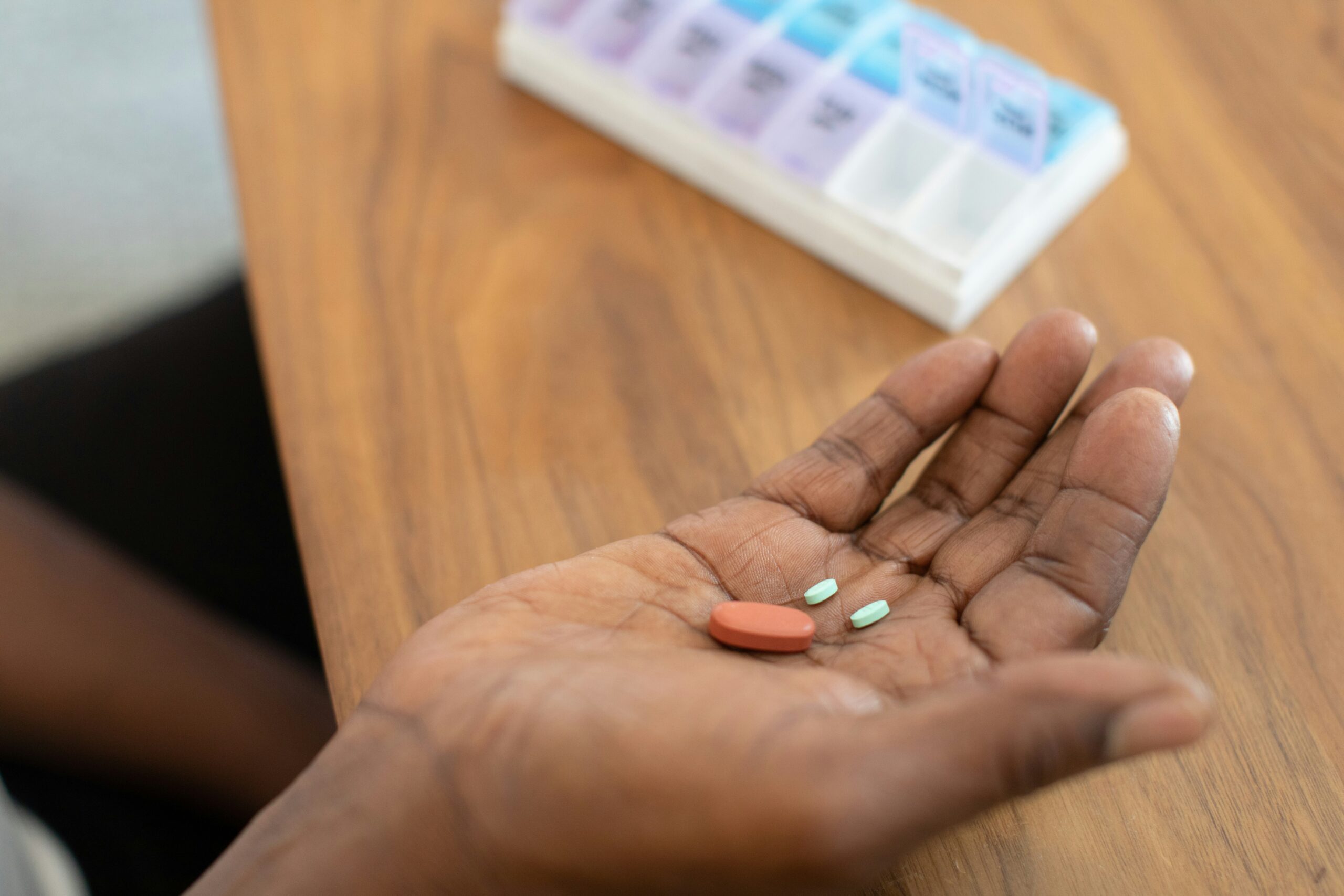 A hand rests facing up on a table with three pills in the palm