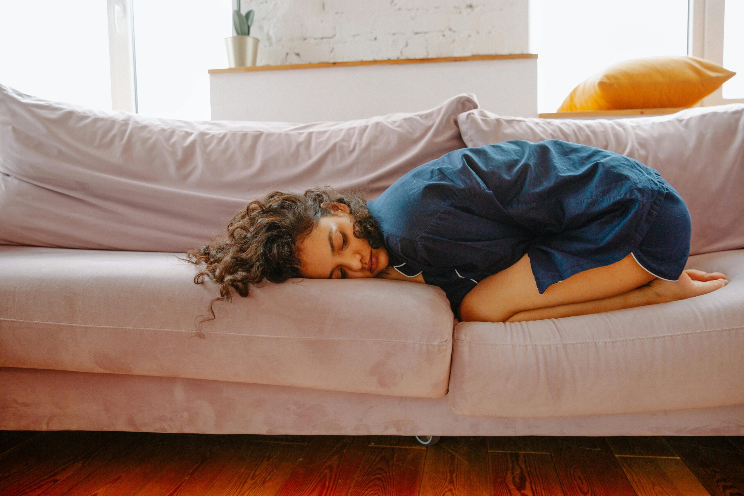 A woman lies on a sofa curled up in a ball