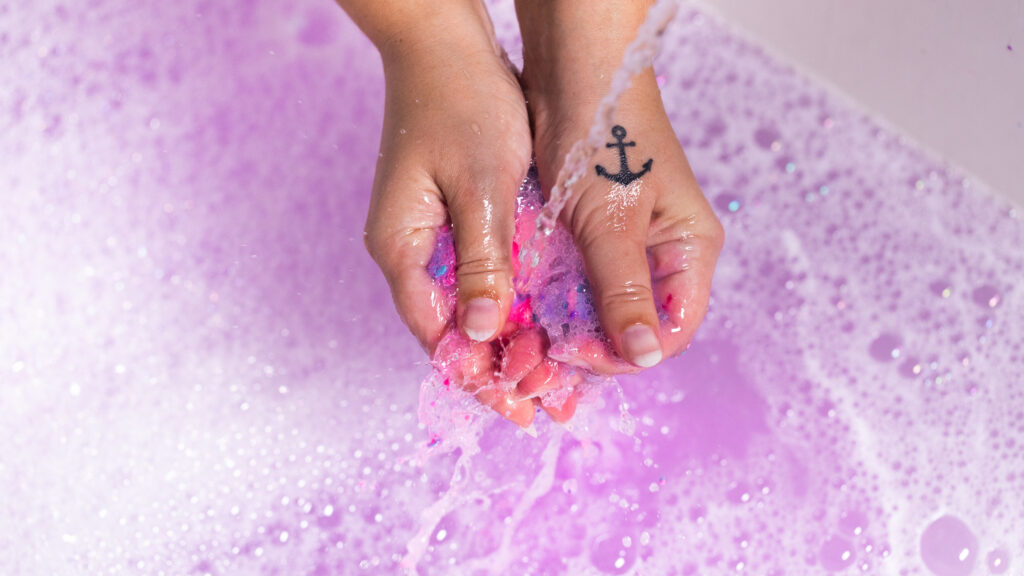Hands crumble Lush Sleepy bubble bar into bath water, turning it purple