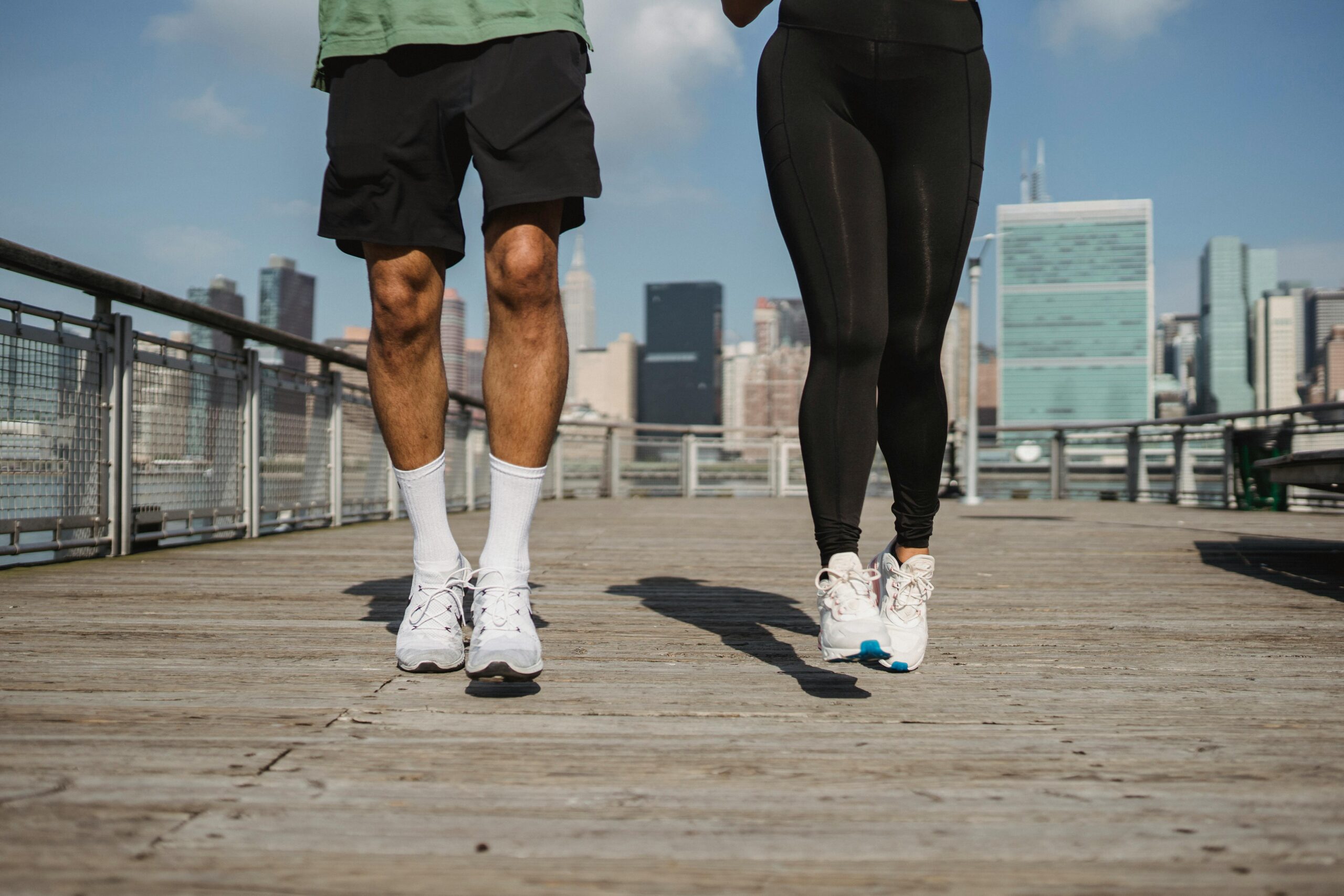 A man and woman are jogging on wooden decking side by side, photographed from the waist down
