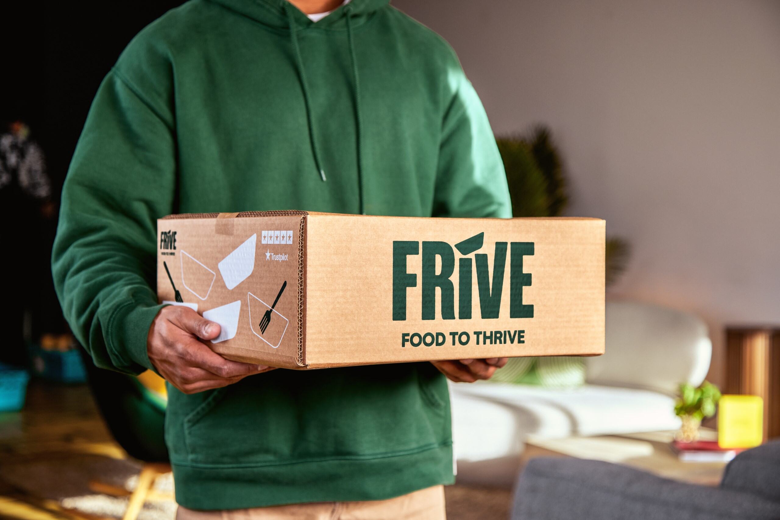 A man in a green hoodie holds a carboard box with Frive written on it also in green