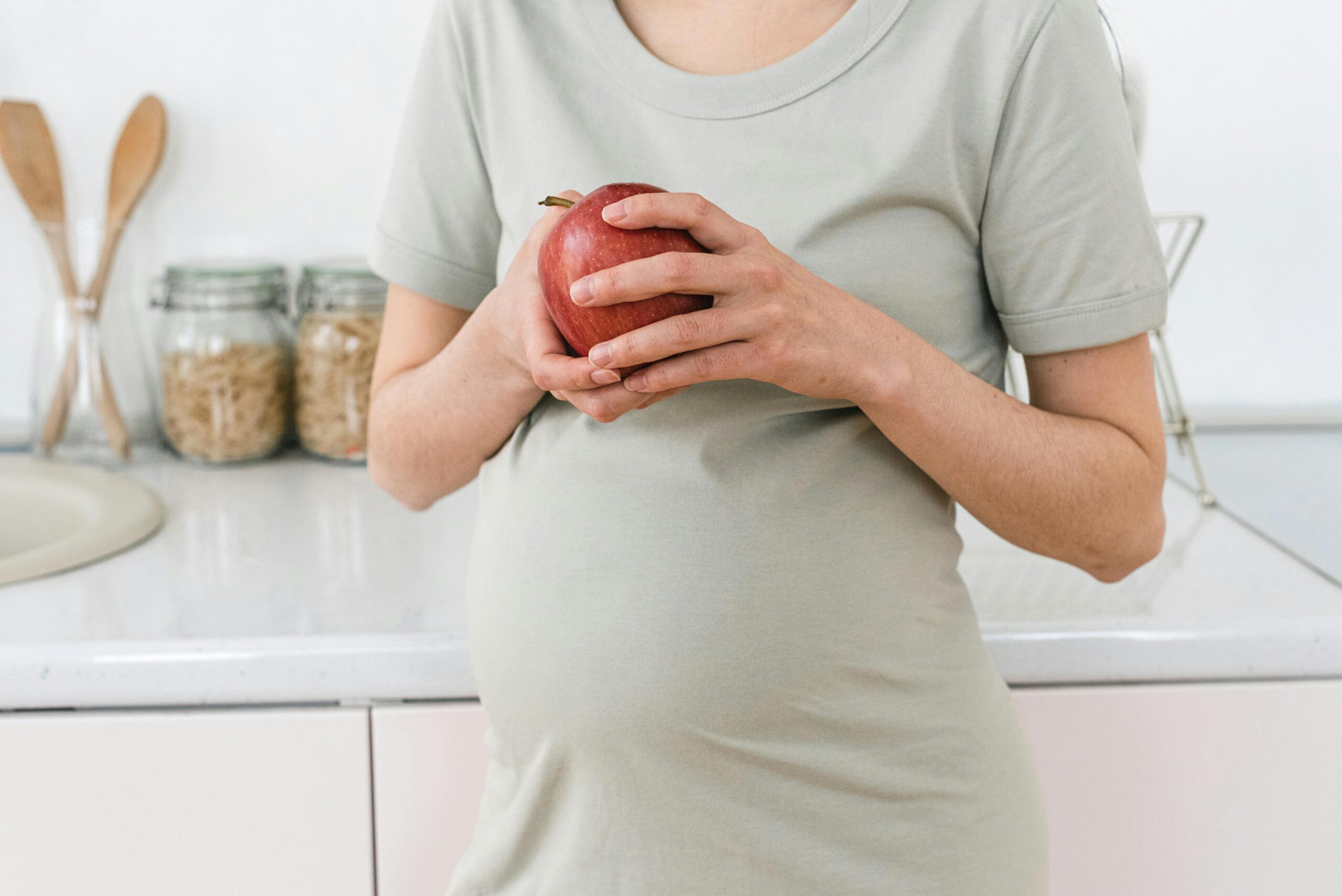 close up of pregnant woman resting an apple on her stomach 