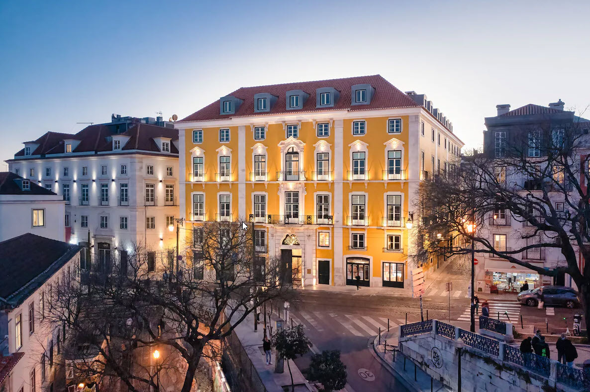 The outside of the yellow building of Palacio Ludovice hotel is Lisbon, at sunset