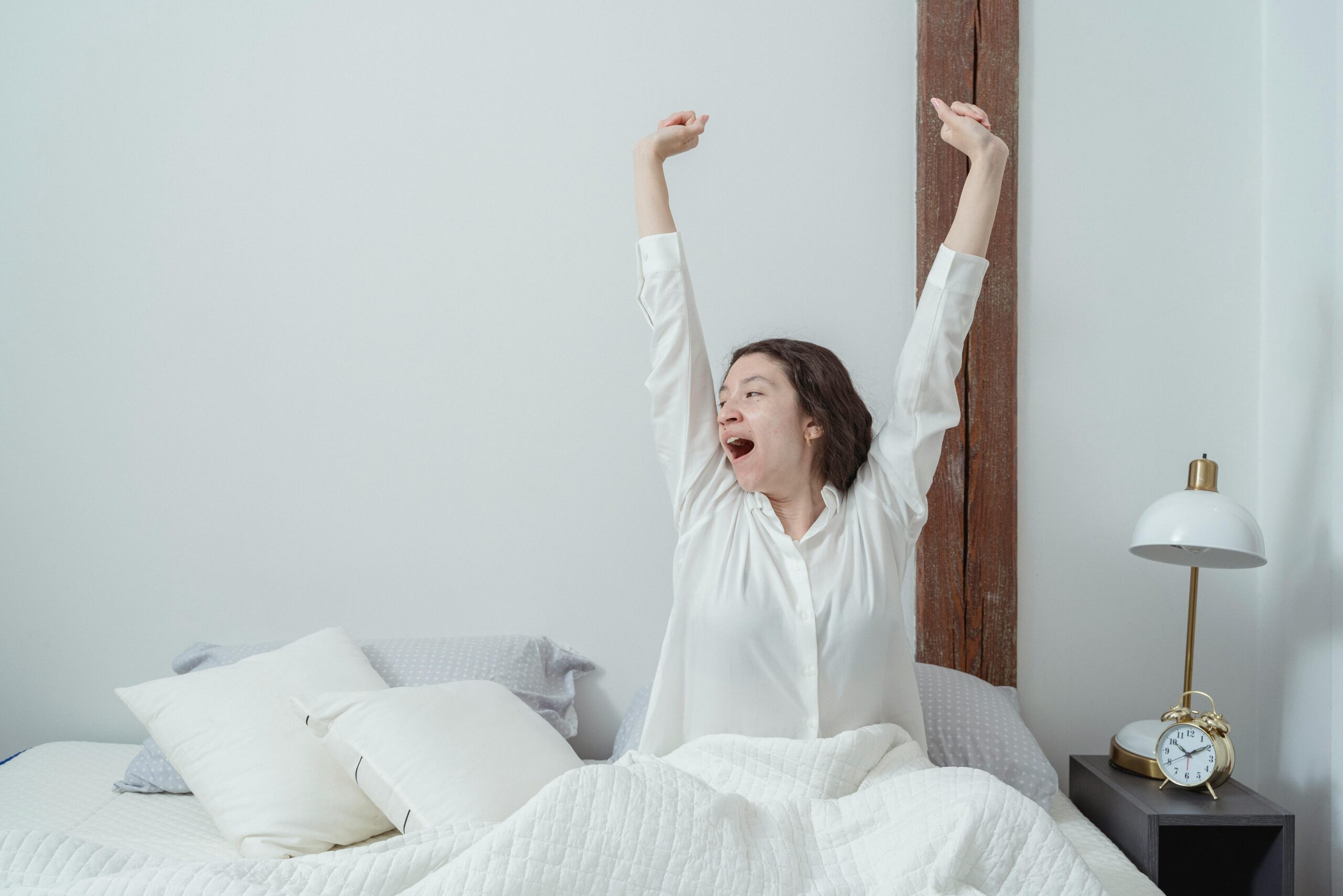 Woman sits in bed stretching and yawning