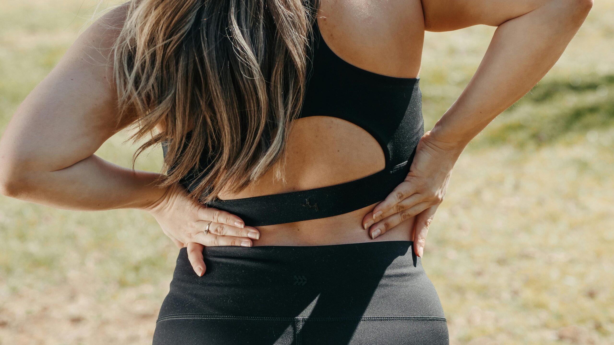 Close up of a woman's back wearing sports bra, rubbing it in pain 