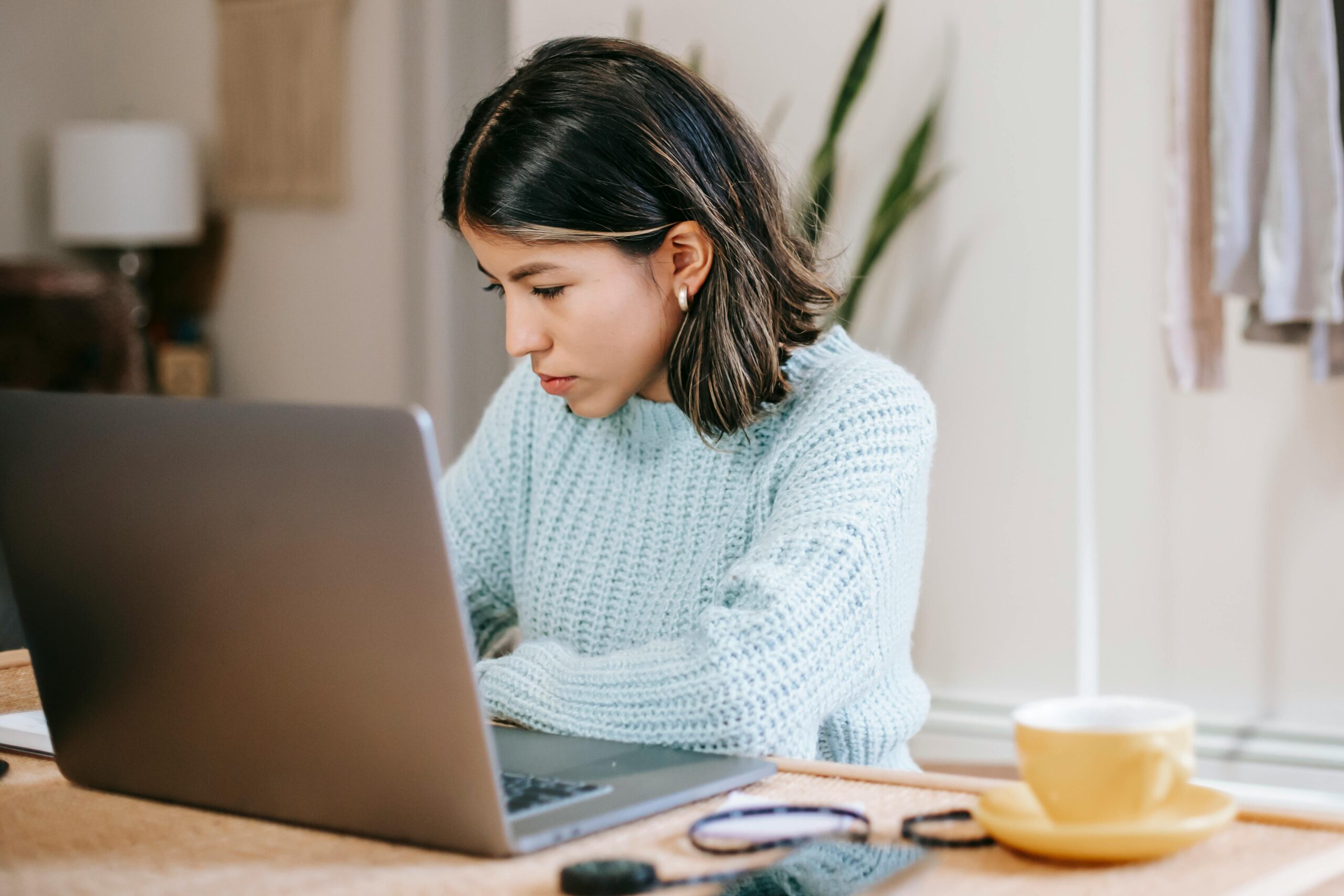 A woman writes something while sitting in front of a laptop