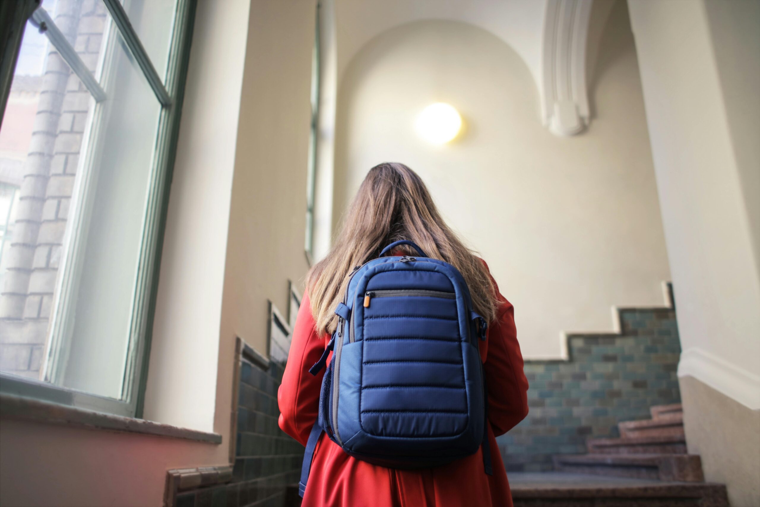 a woman faces away looking at stairs with a backpack on