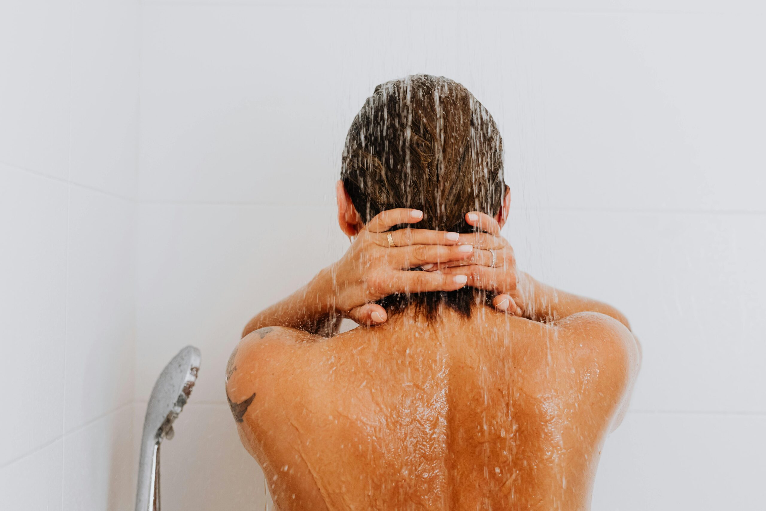 a woman washes shampoo out of her hair in the shower facing away 