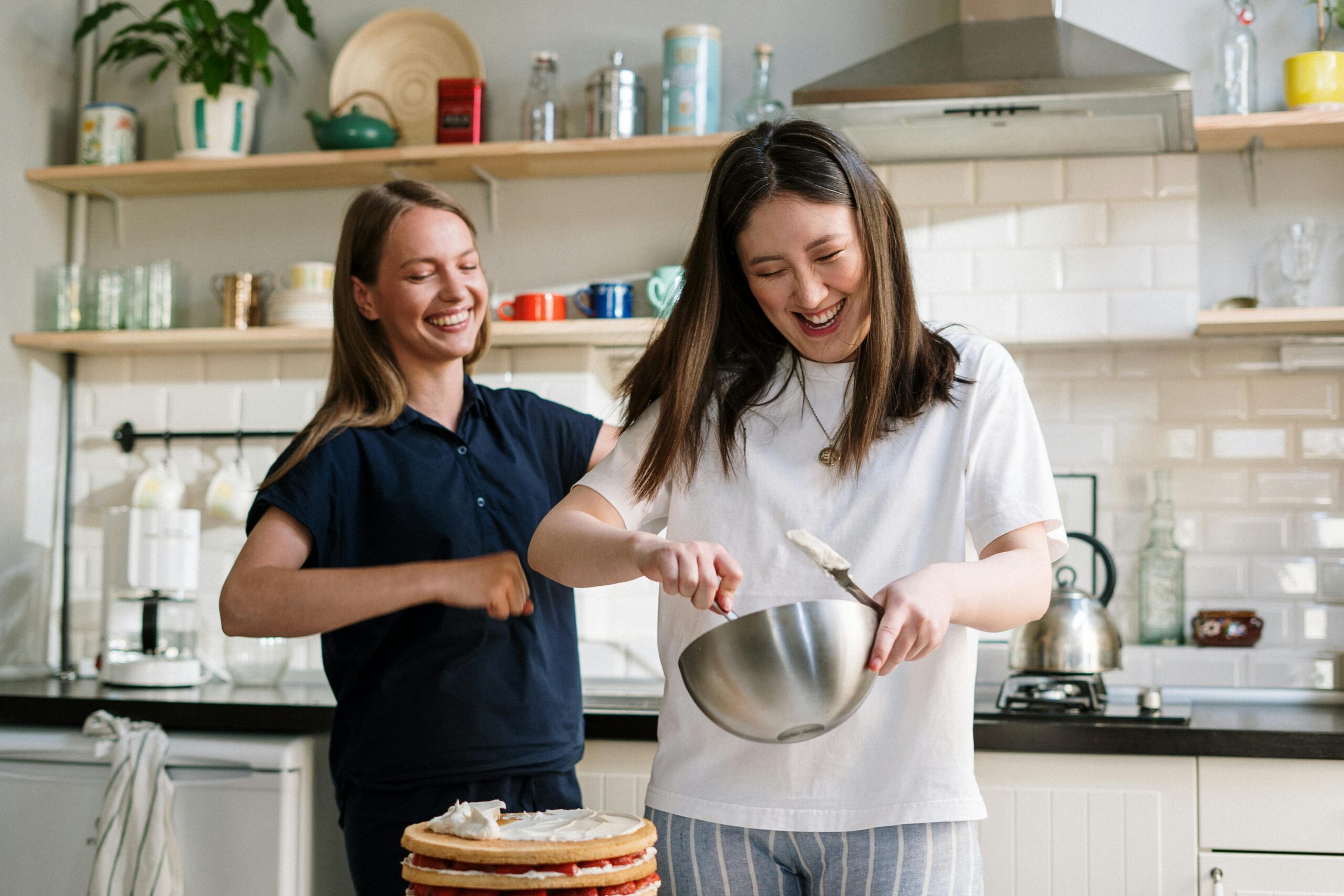 Two woman baking a cake and laughing together in a kitchen