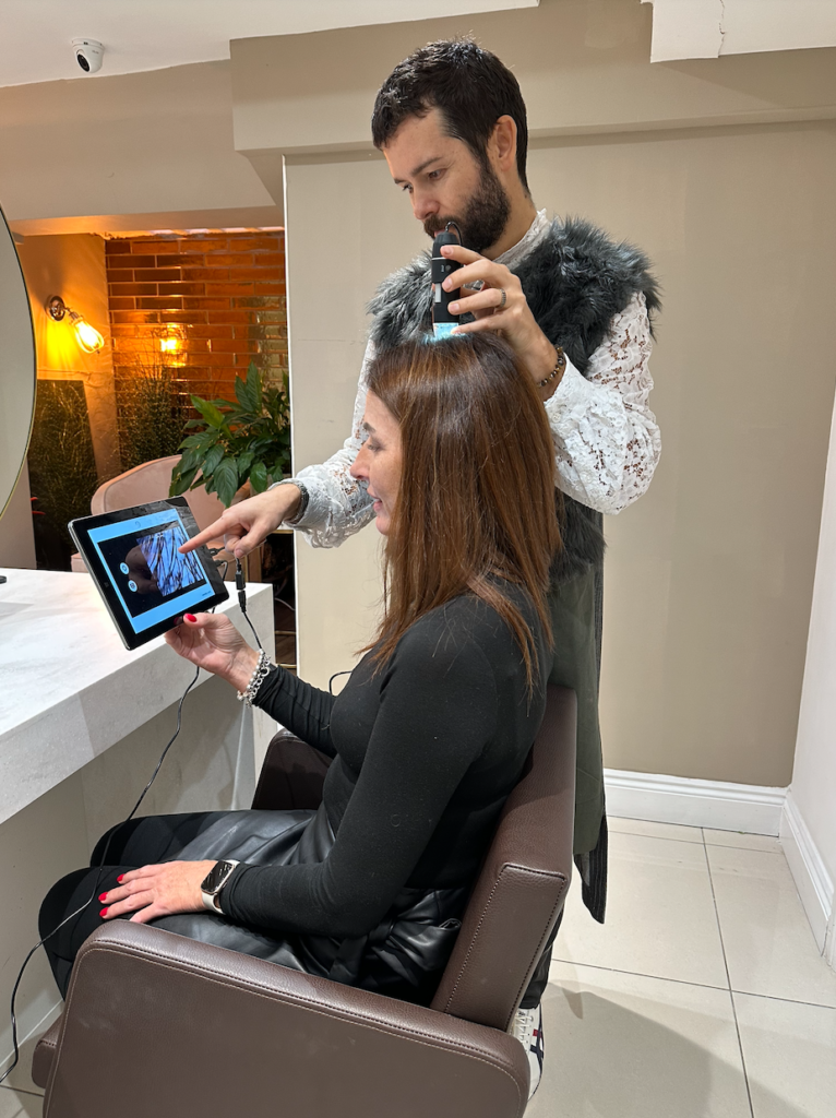 A male hair stylist looks at a woman's scalp with a microscopic camera 