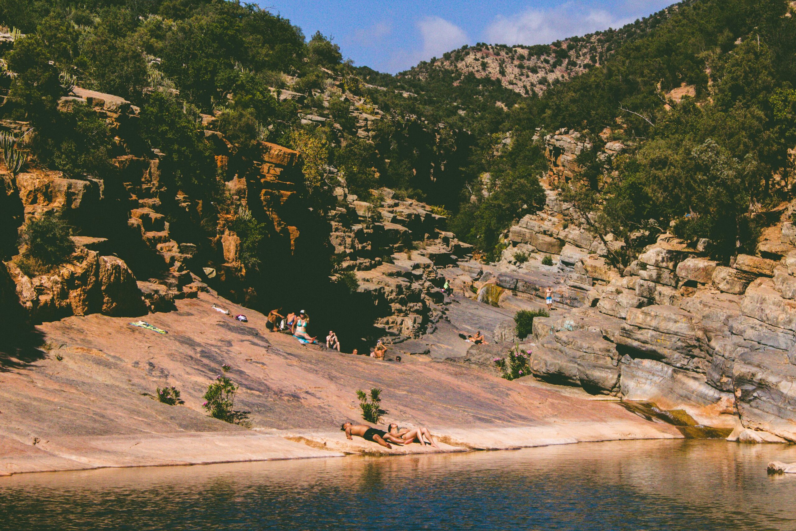 People sunbathing on rocks by water in Paradise Valley, Morocco